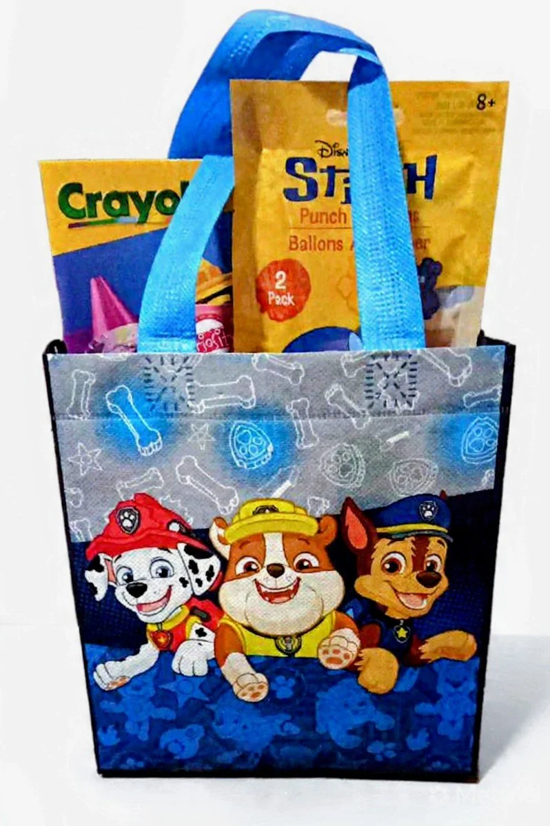 A gift bag with a Paw Patrol design featuring three animated puppies, along with party supplies inside, including a Crayola coloring book and Disney's Stretch Punch balloons.