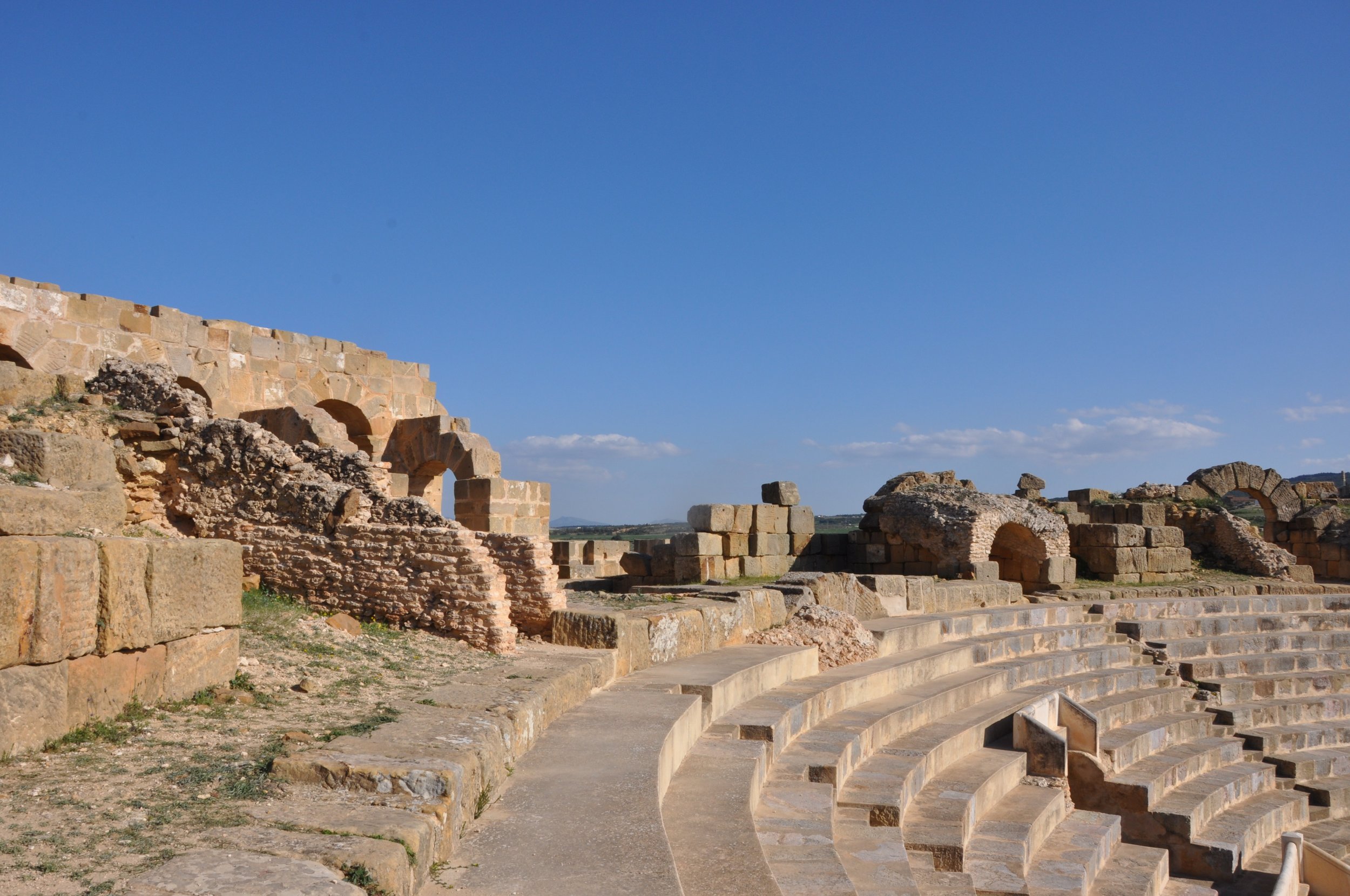 Ancient Roman amphitheater ruins with stone arches and benches under a clear blue sky.