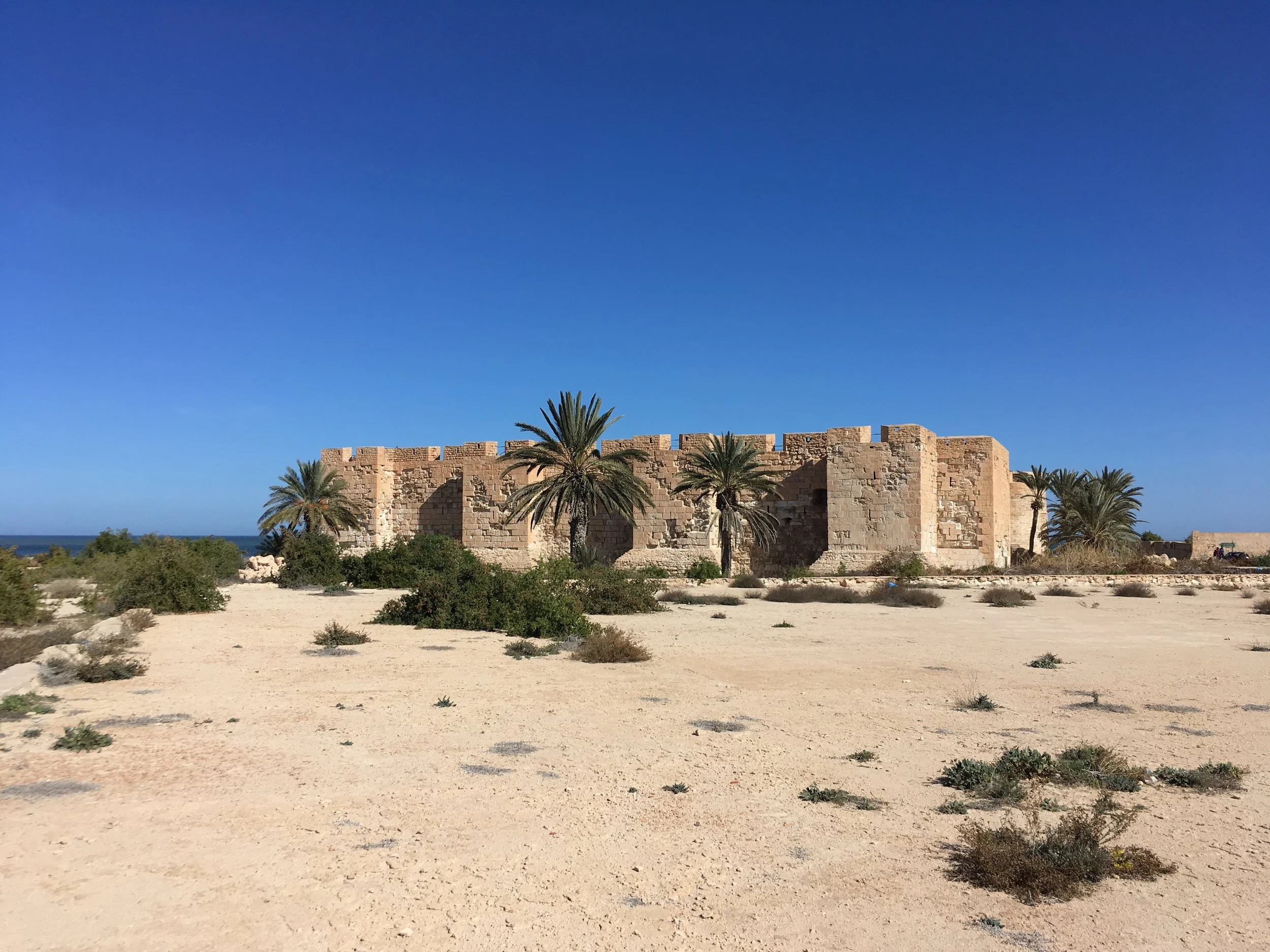 Ancient stone ruins with arches and a palm tree against a clear blue sky.