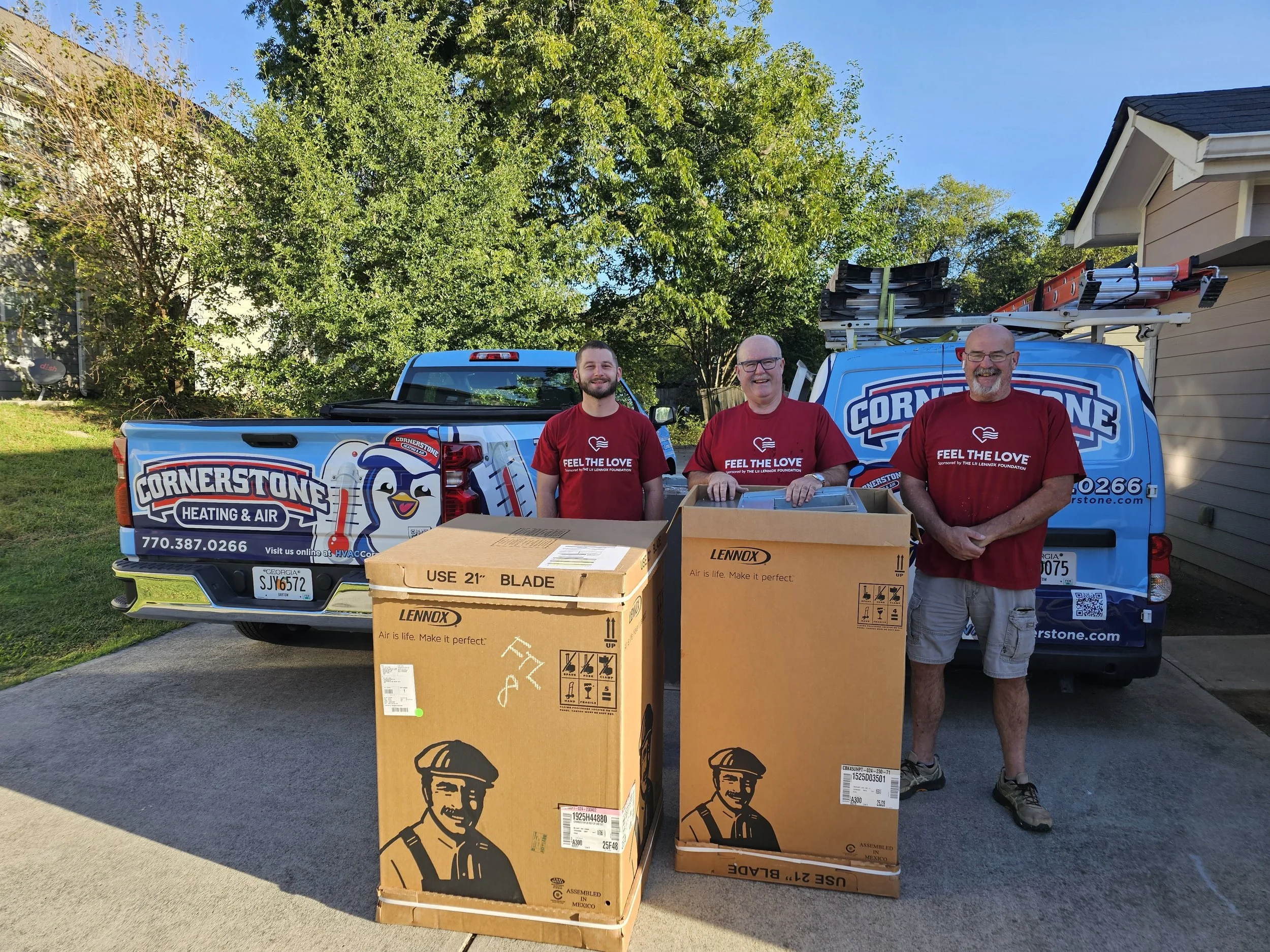 Three men standing outdoors, smiling, next to a vehicle with a logo of a penguin wearing a hard hat for Cornerstone Heating & Air, with boxes in front of them.
