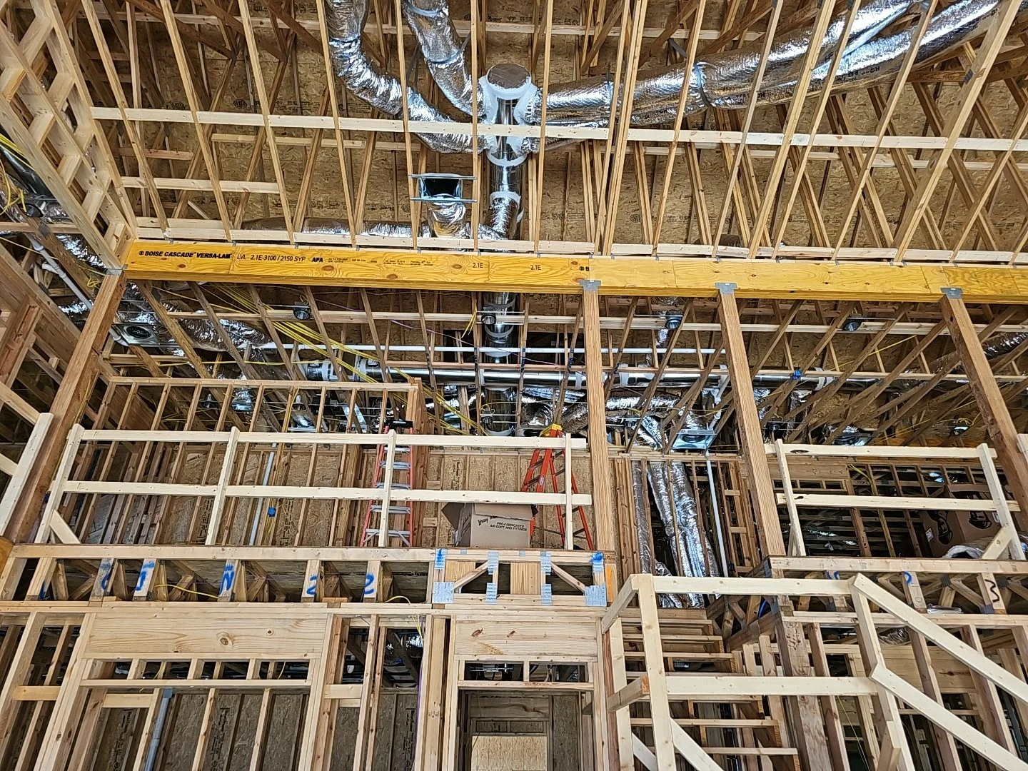 Interior view of a building under construction with exposed wooden framework, metal ductwork, and construction ladders.