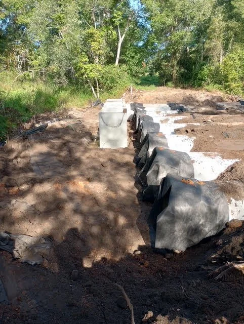 Construction site with covered drainage pipes and concrete blocks during daytime, surrounded by green trees.