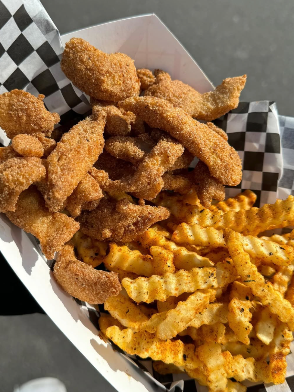 Fried fish and crinkle-cut French fries in checkered paper container