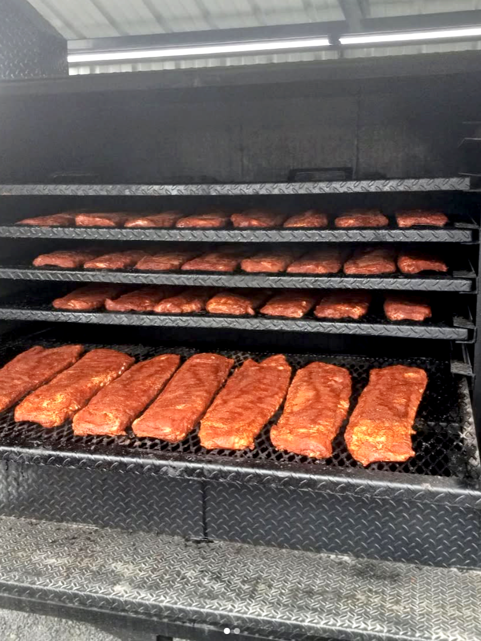 Meat slabs cooking on a smoker grill with multiple racks of beef briskets.