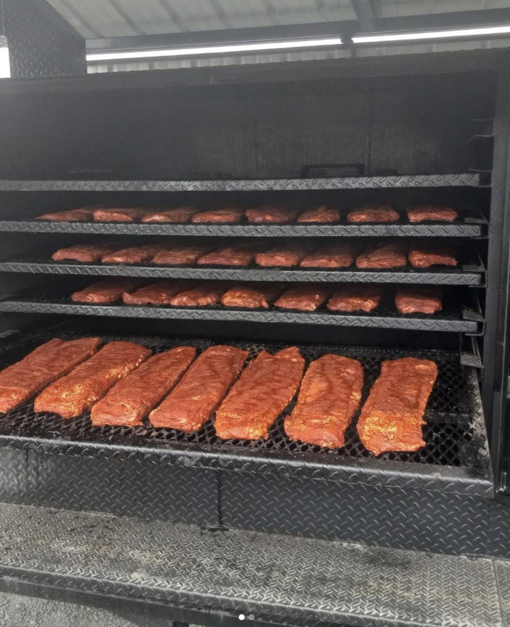 Meat racks with seasoned ribs cooking on a smoker