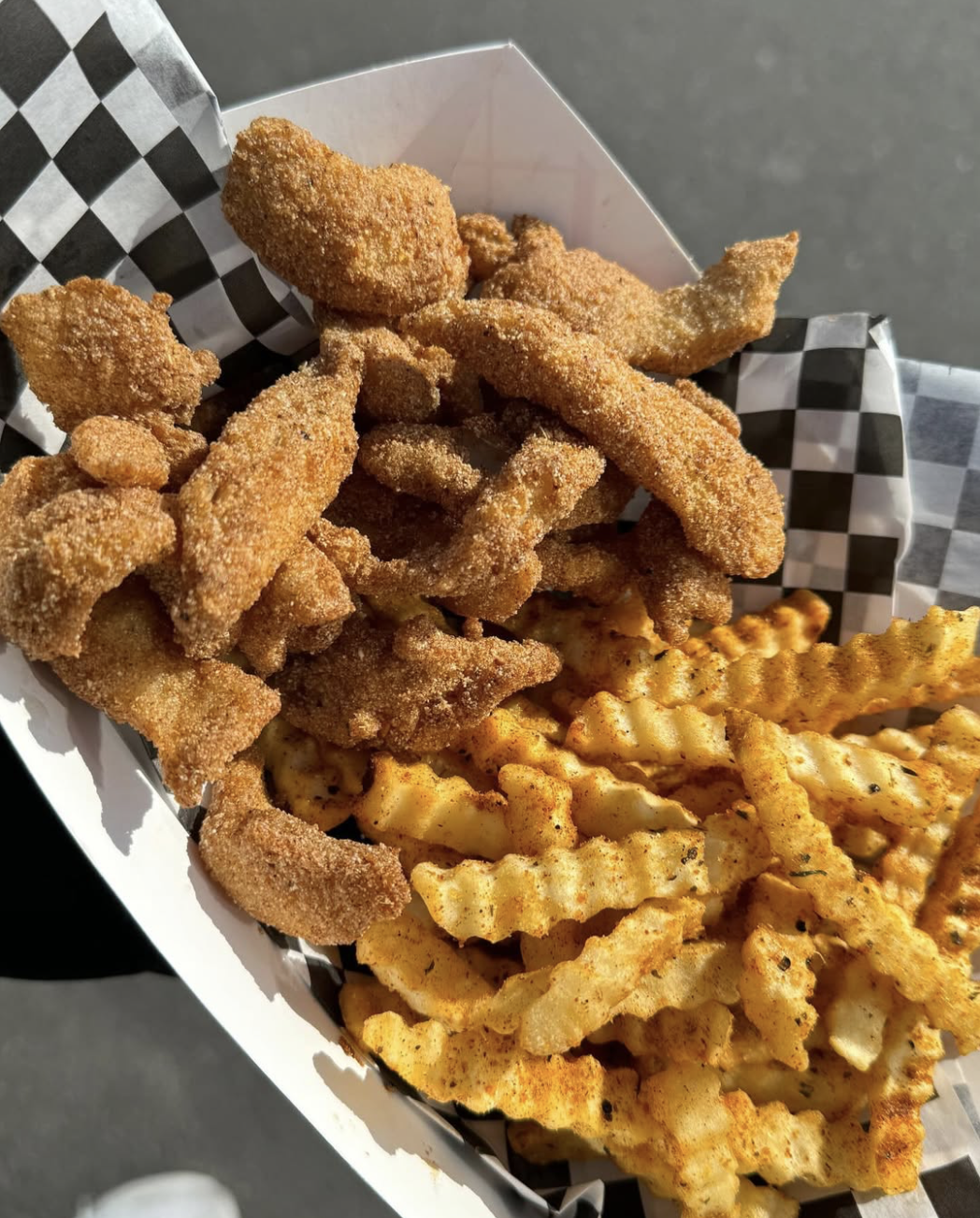 Fried chicken tenders and crinkle-cut fries in a checkered paper tray.