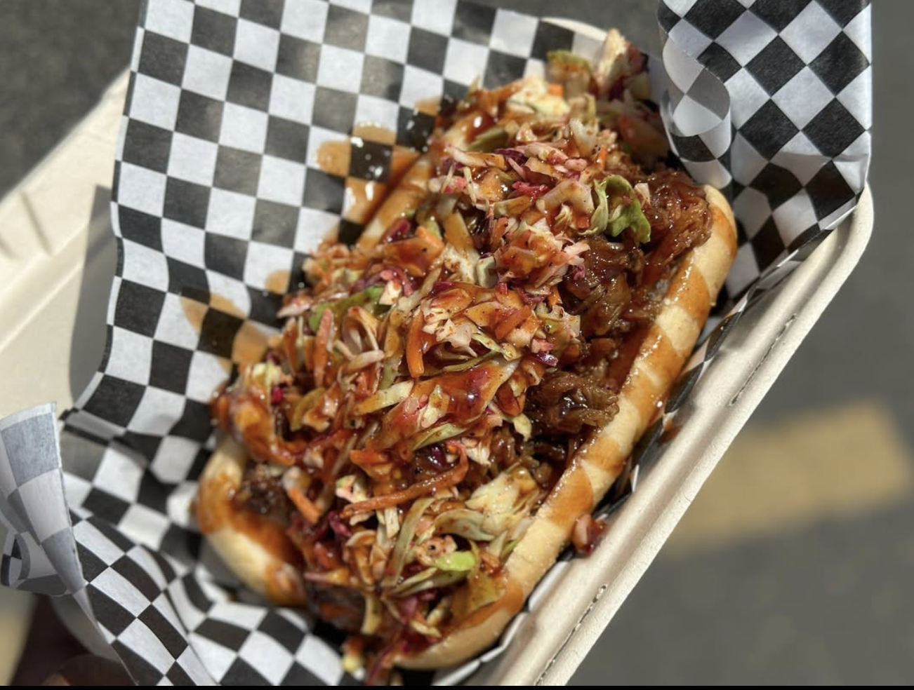Close-up of a hot dog topped with shredded cole slaw and barbecue sauce in a checkered paper-lined basket.