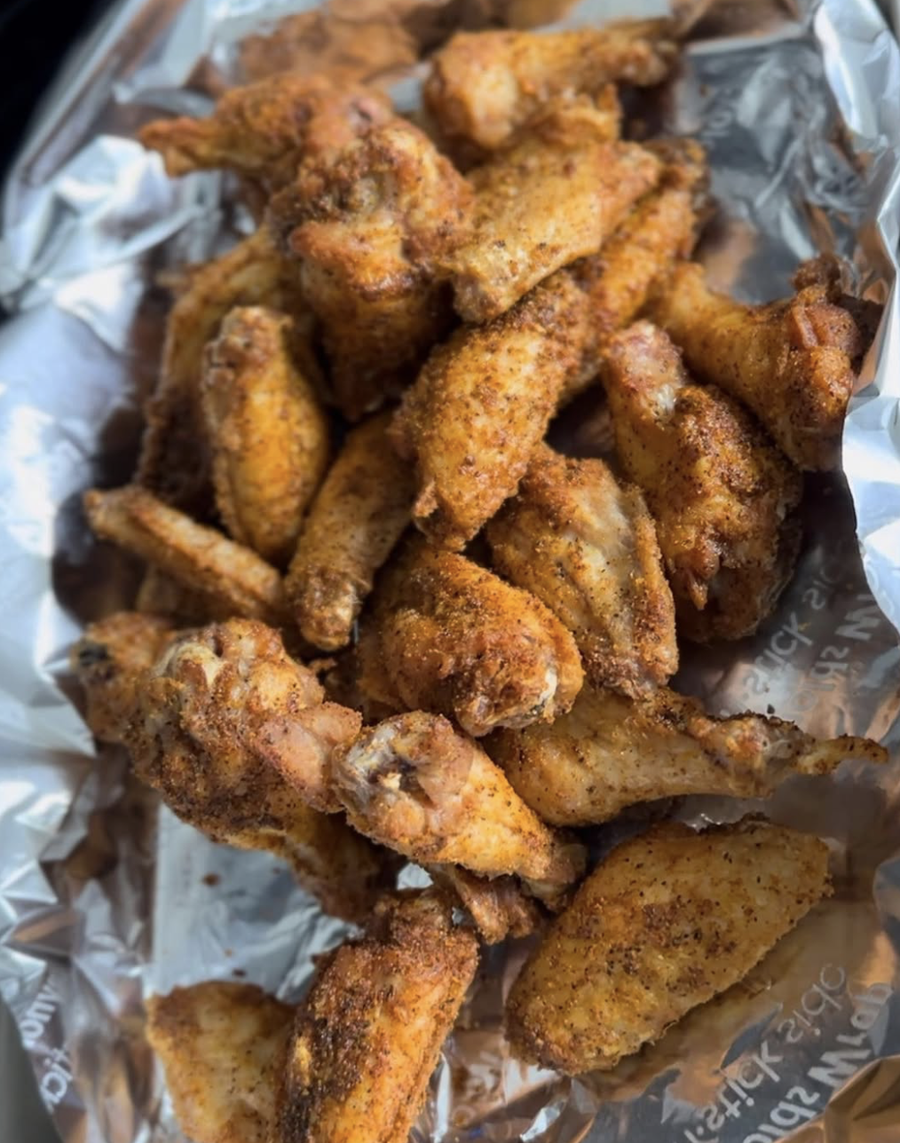 Close-up of seasoned fried chicken wings and drumsticks in a basket lined with foil.