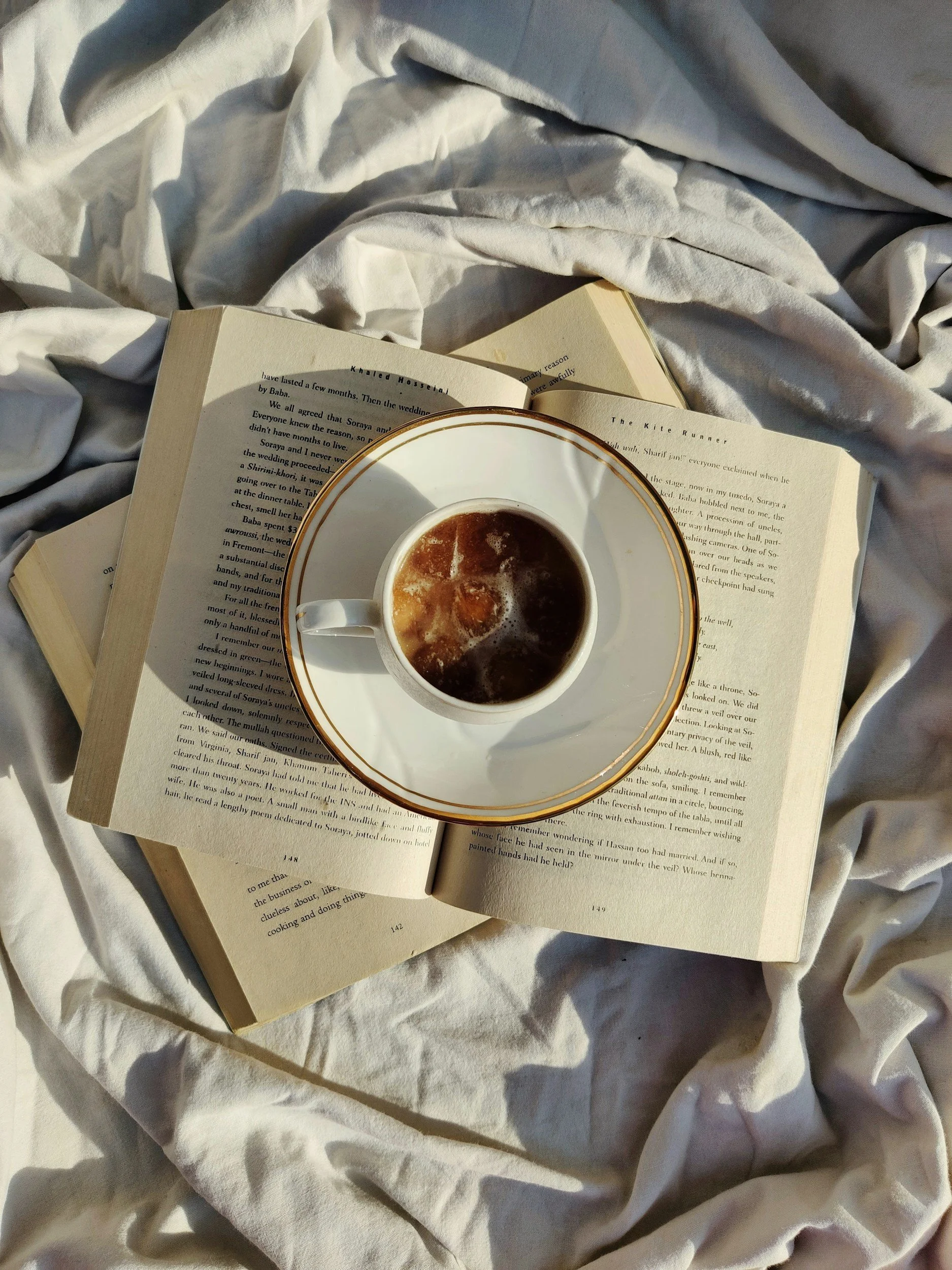 Open book with a cup of coffee placed on top, resting on a white creased cloth.