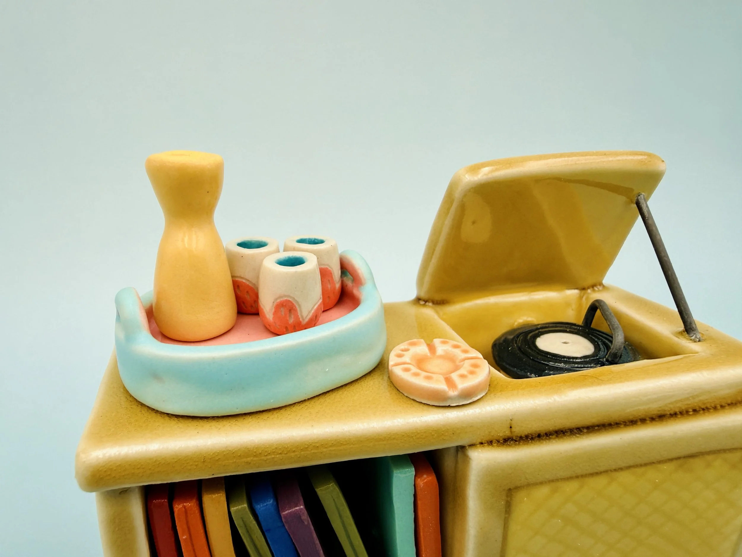 Ceramic figurine of a vintage record player with colorful record spines and a tray holding a yellow vase and decorative Malenka Made miniature pink tumblers.