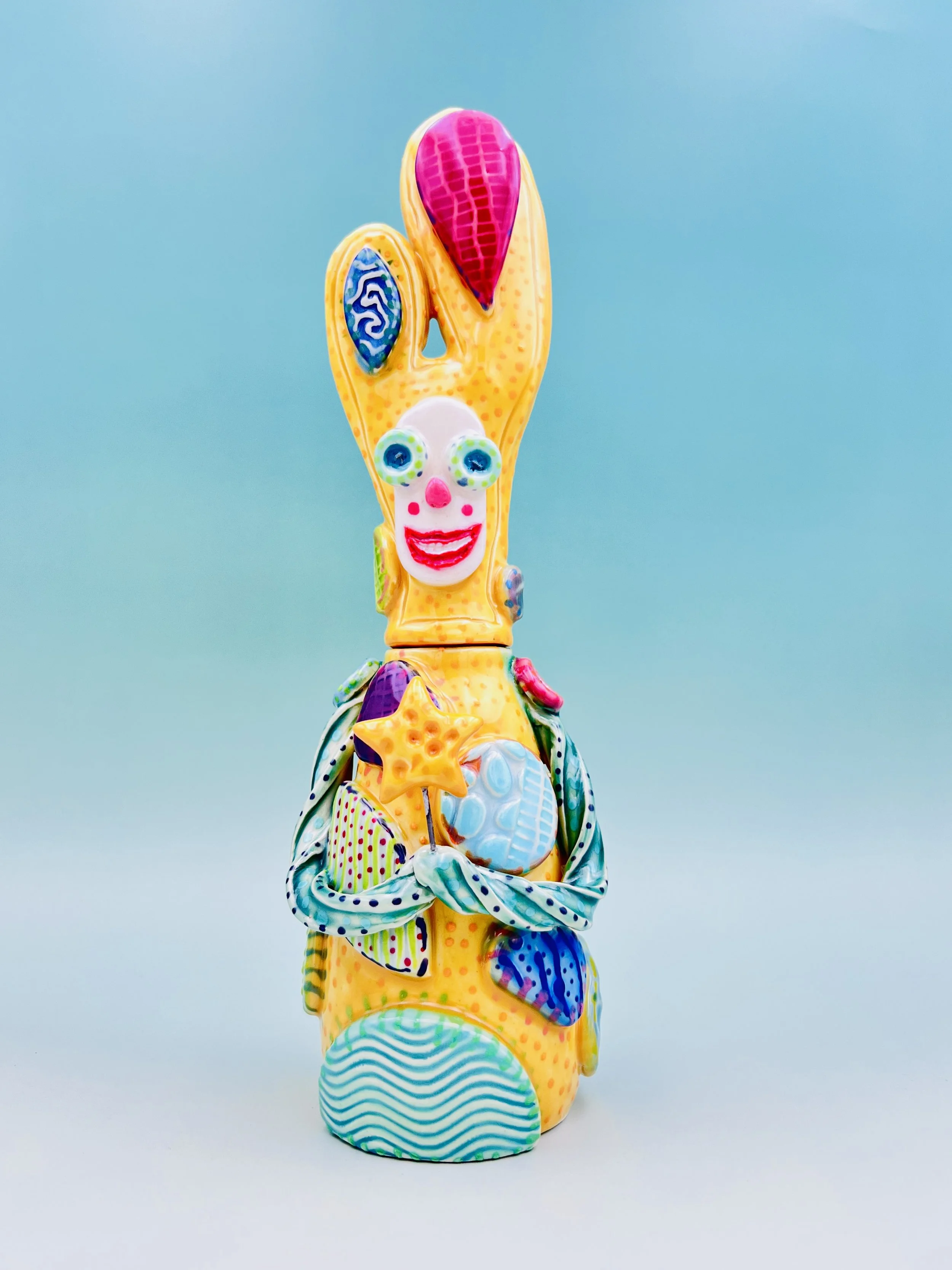 Colorful, whimsical ceramic figures called Gimmies with exaggerated facial features and various patterns, set against a gradient pastel background.