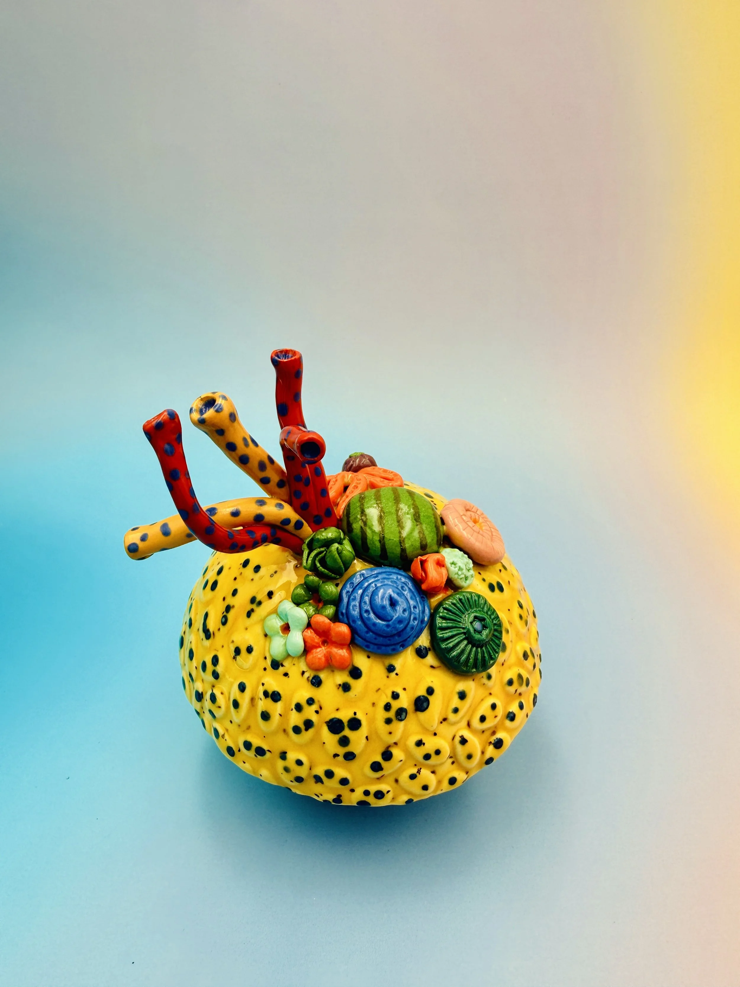 Colorful, textured clay sculptures resembling coral reefs arranged on a gradient background. Each piece has vibrant, intricate details, evoking a sense of ocean life.