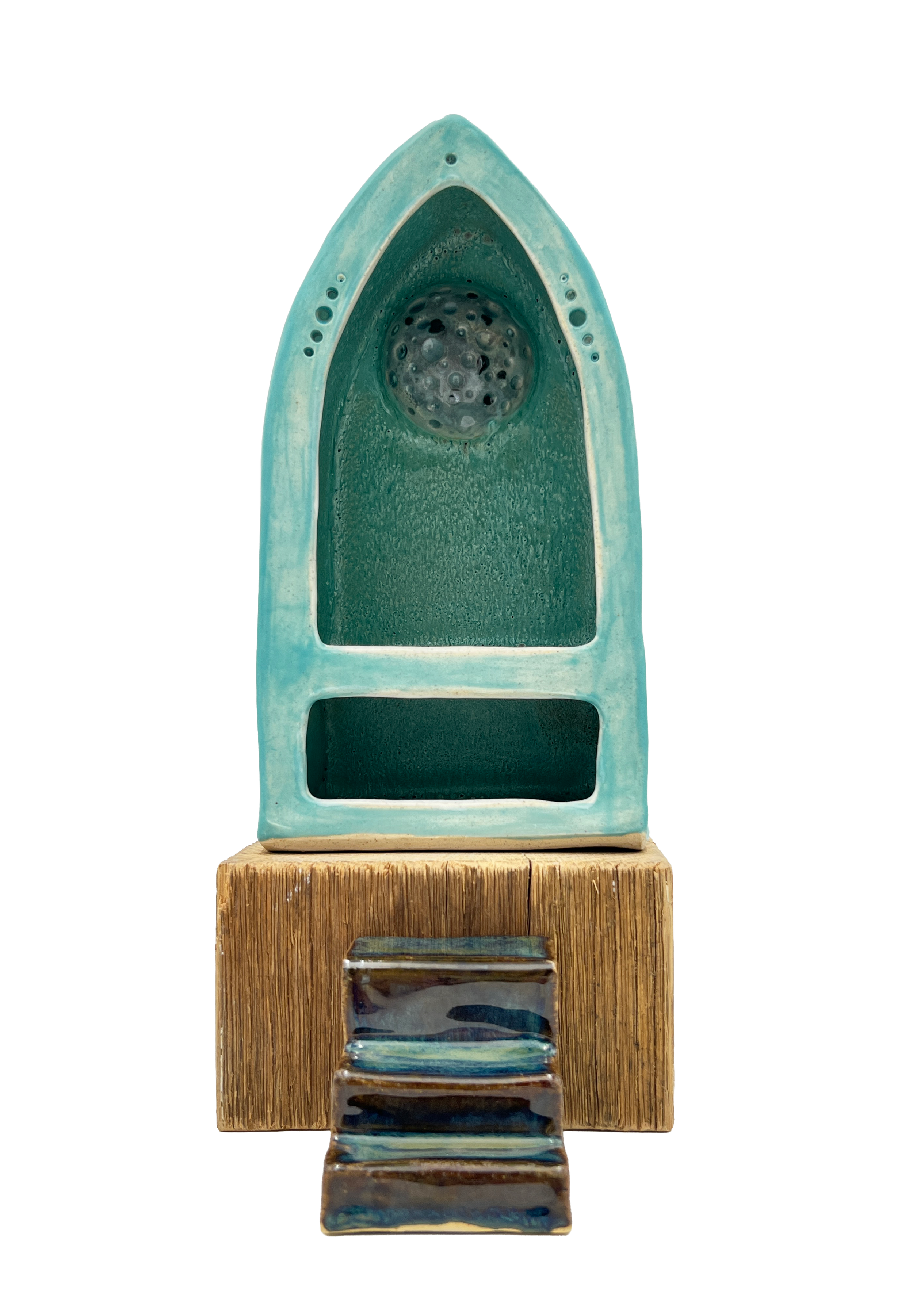Ceramic sculpture featuring a teal arched niche with a perforated circular element, a rectangular opening, a textured tan base, and a small stairway in front.