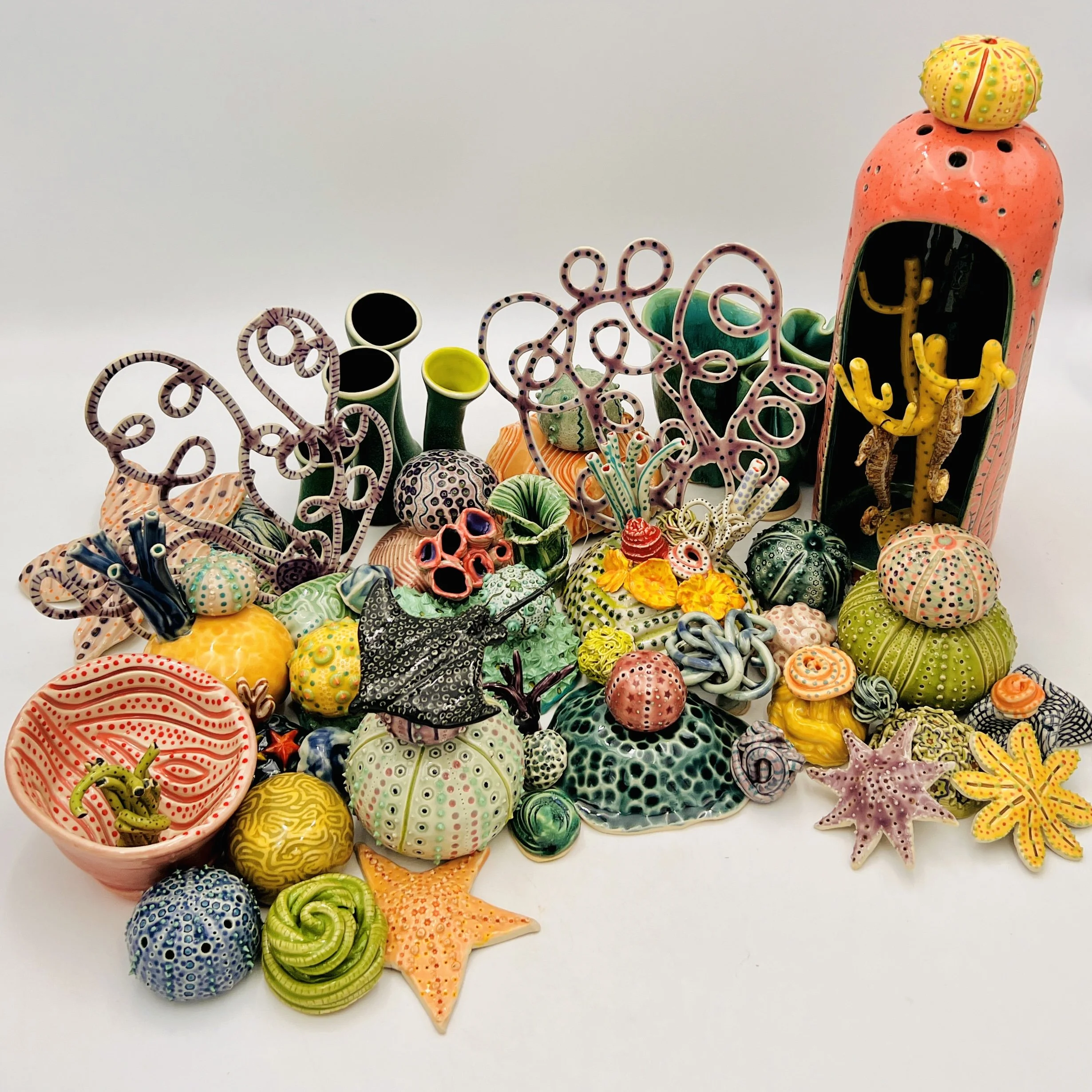 Colorful, textured clay sculptures resembling coral reefs arranged on a gradient background. Each piece has vibrant, intricate details, evoking a sense of ocean life.