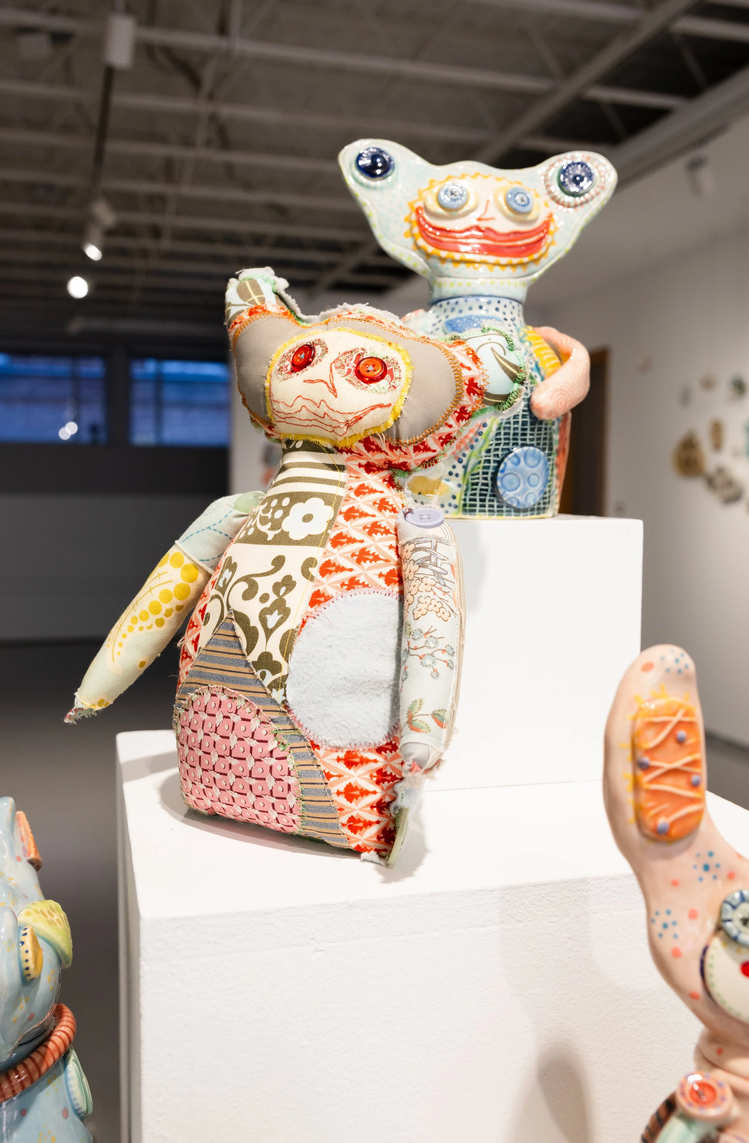 Colorful, hand-decorated animal sculptures stand on white pedestals in a modern gallery, creating a playful, whimsical exhibition against a gray wall.