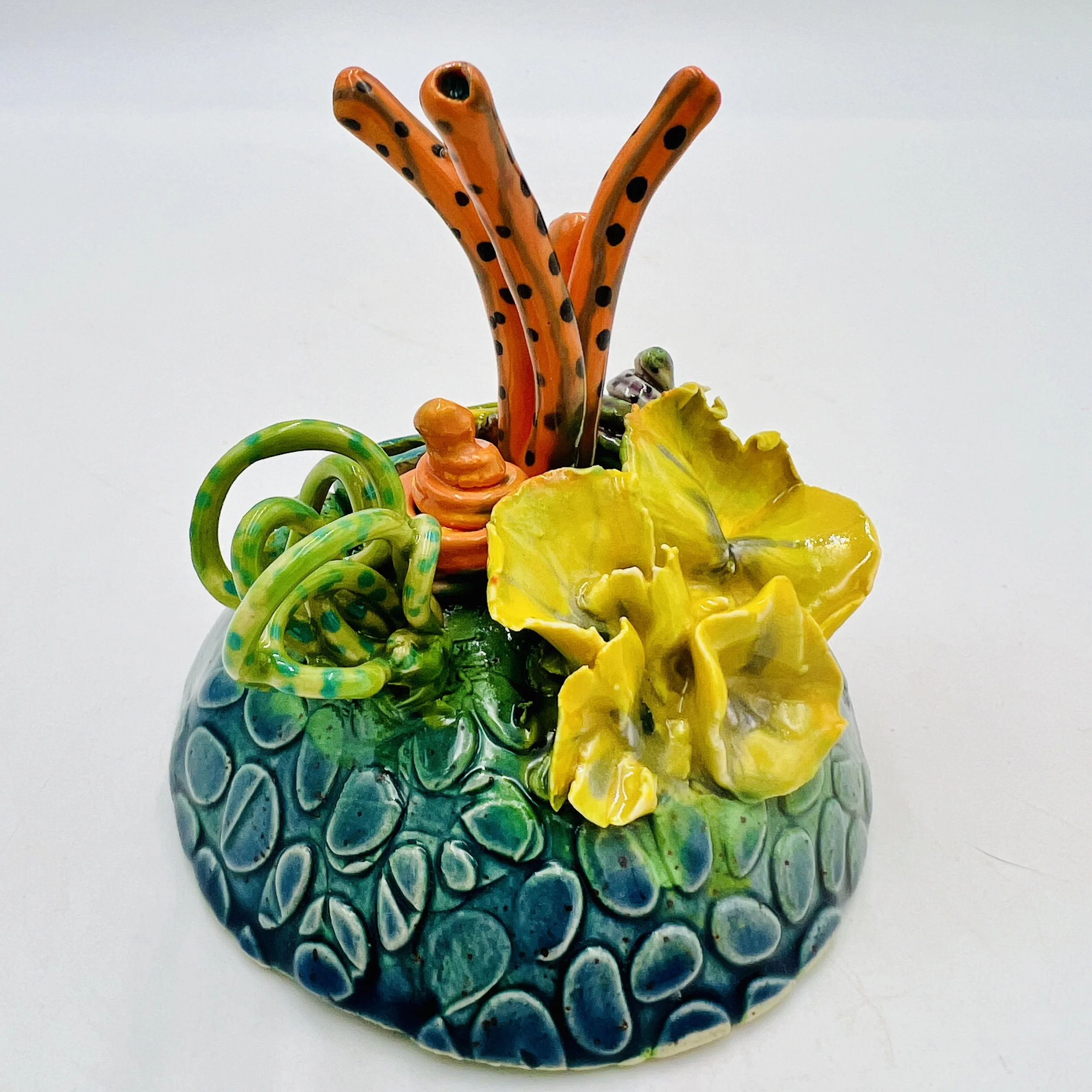 Colorful, textured clay sculptures resembling coral reefs arranged on a gradient background. Each piece has vibrant, intricate details, evoking a sense of ocean life.