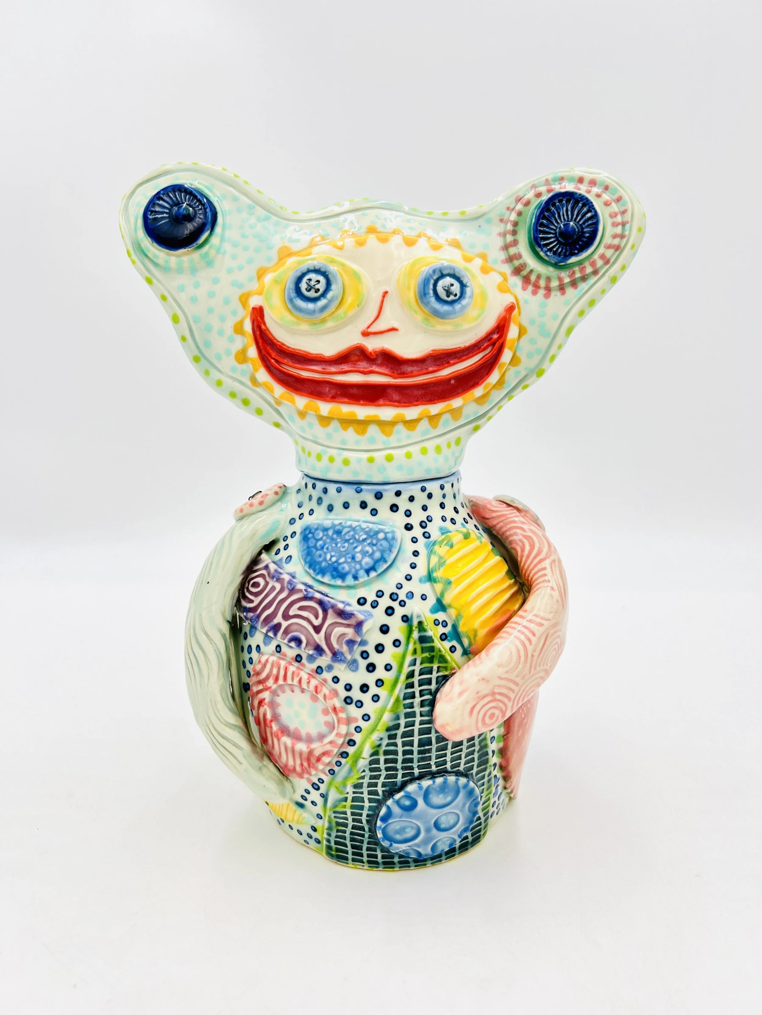 Colorful, whimsical ceramic figures called Gimmies with exaggerated facial features and various patterns, set against a gradient pastel background.