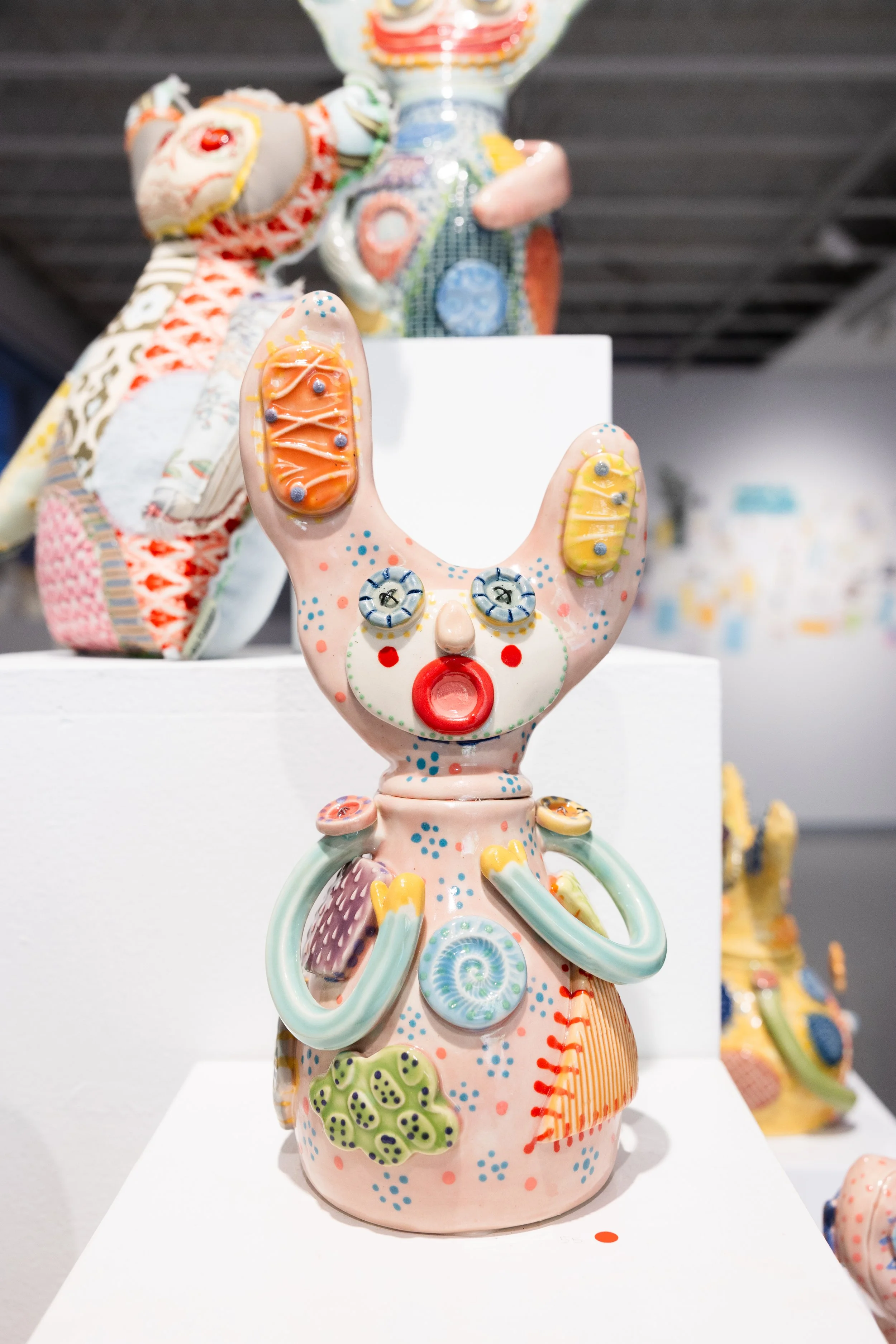 Colorful, hand-decorated animal sculptures stand on white pedestals in a modern gallery, creating a playful, whimsical exhibition against a gray wall.