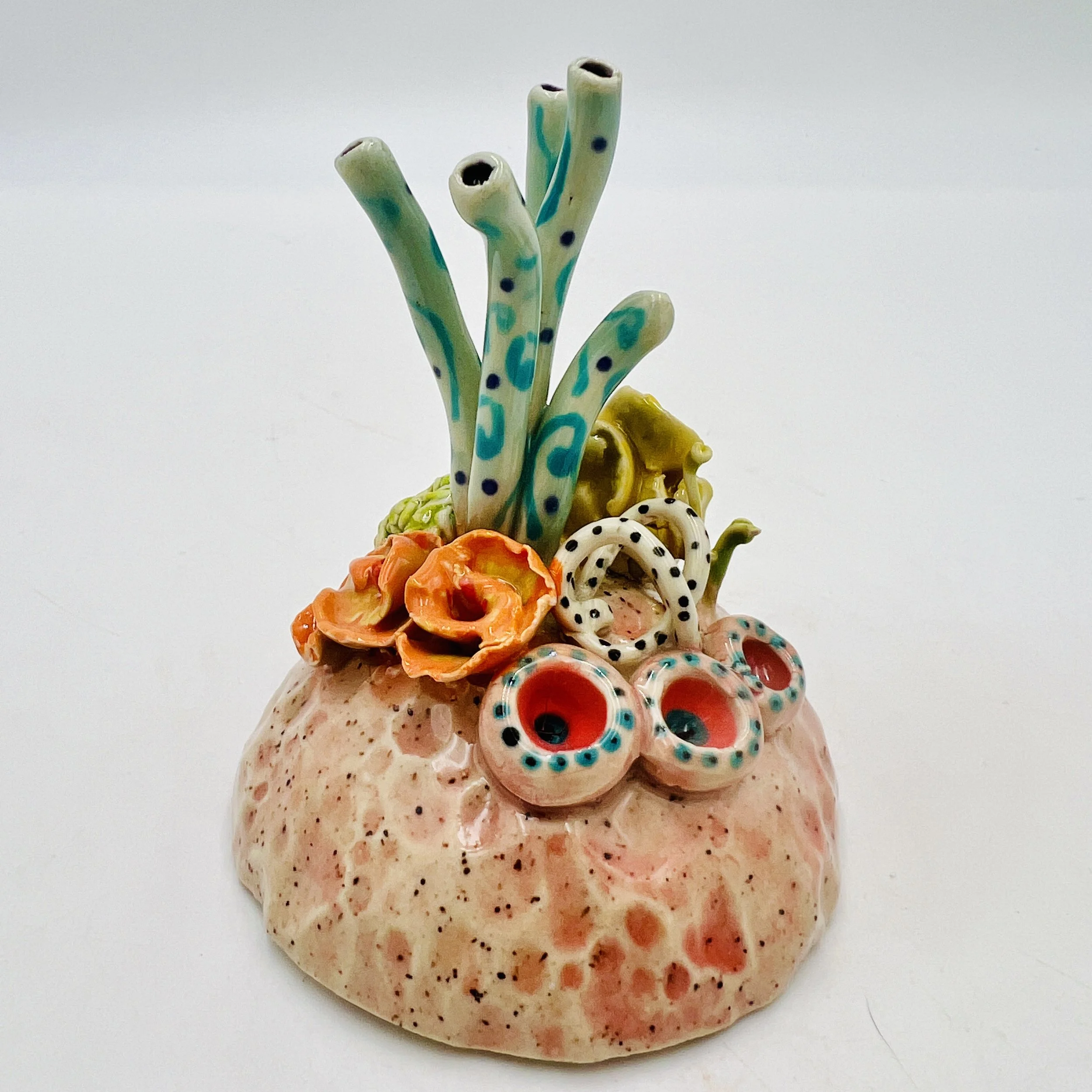 Colorful, textured clay sculptures resembling coral reefs arranged on a gradient background. Each piece has vibrant, intricate details, evoking a sense of ocean life.