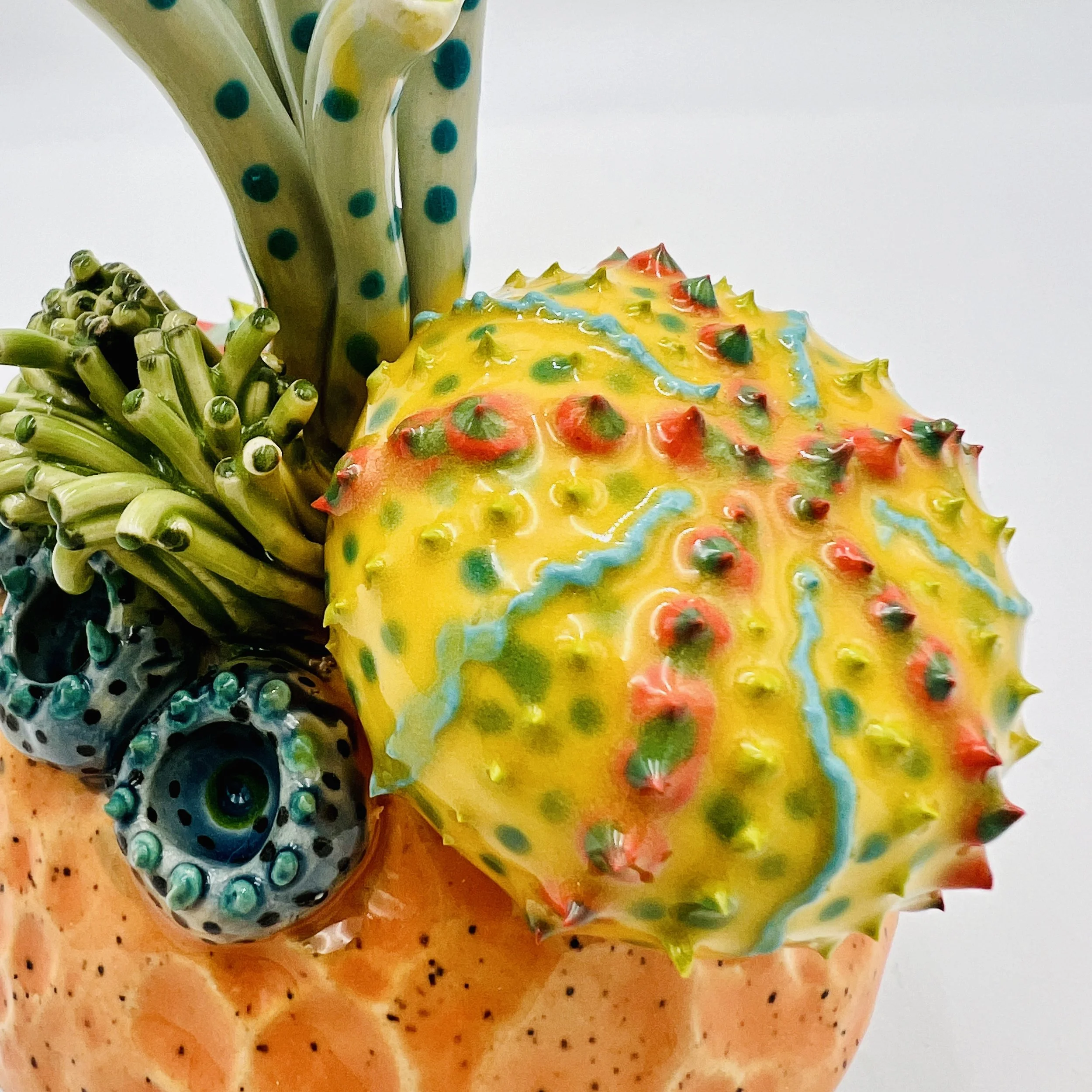 Colorful, textured clay sculptures resembling coral reefs arranged on a gradient background. Each piece has vibrant, intricate details, evoking a sense of ocean life.