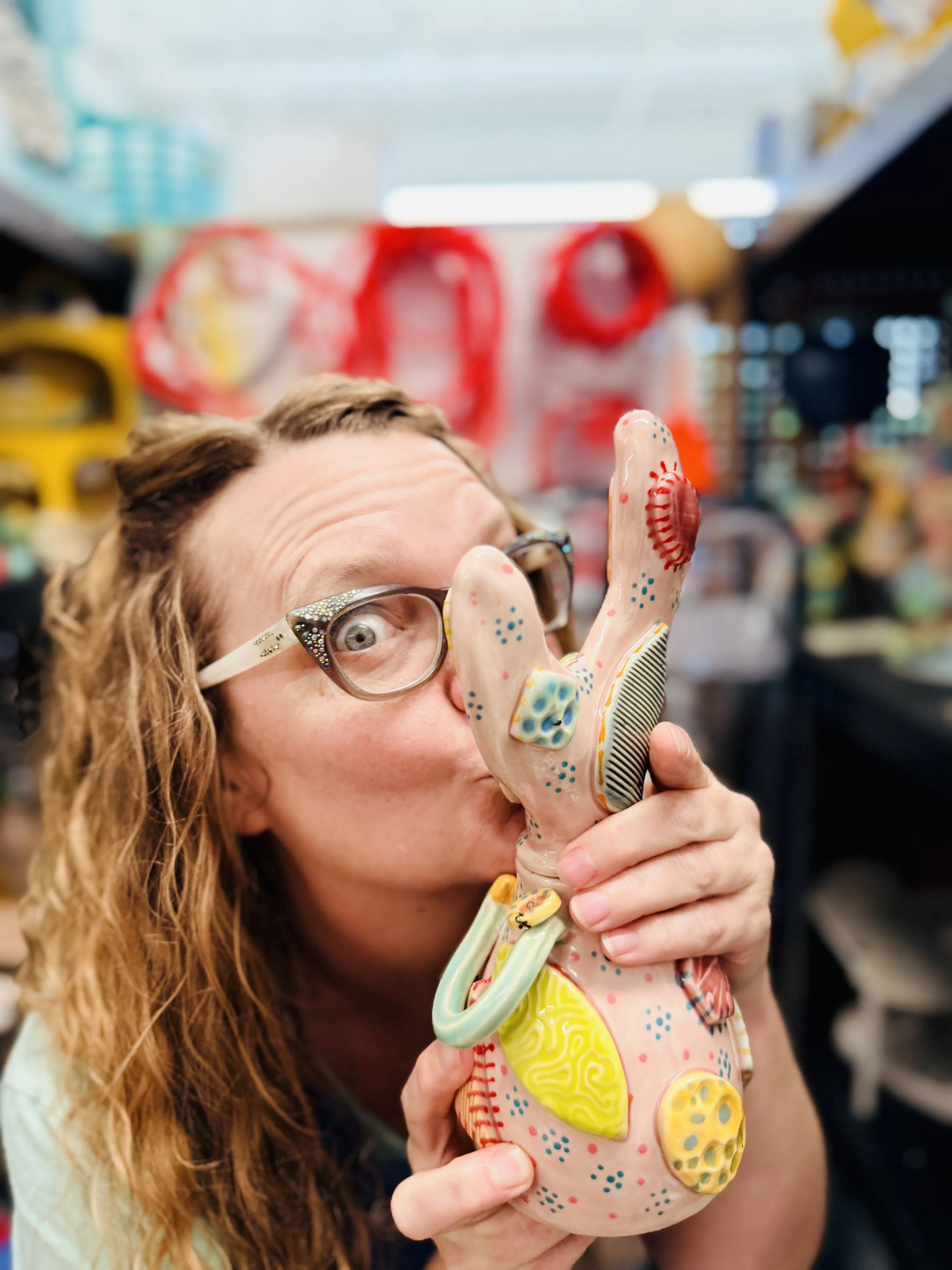 A bespectacled woman affectionately kisses a ceramic gimmie doll, highlighting a charming and lighthearted moment.
