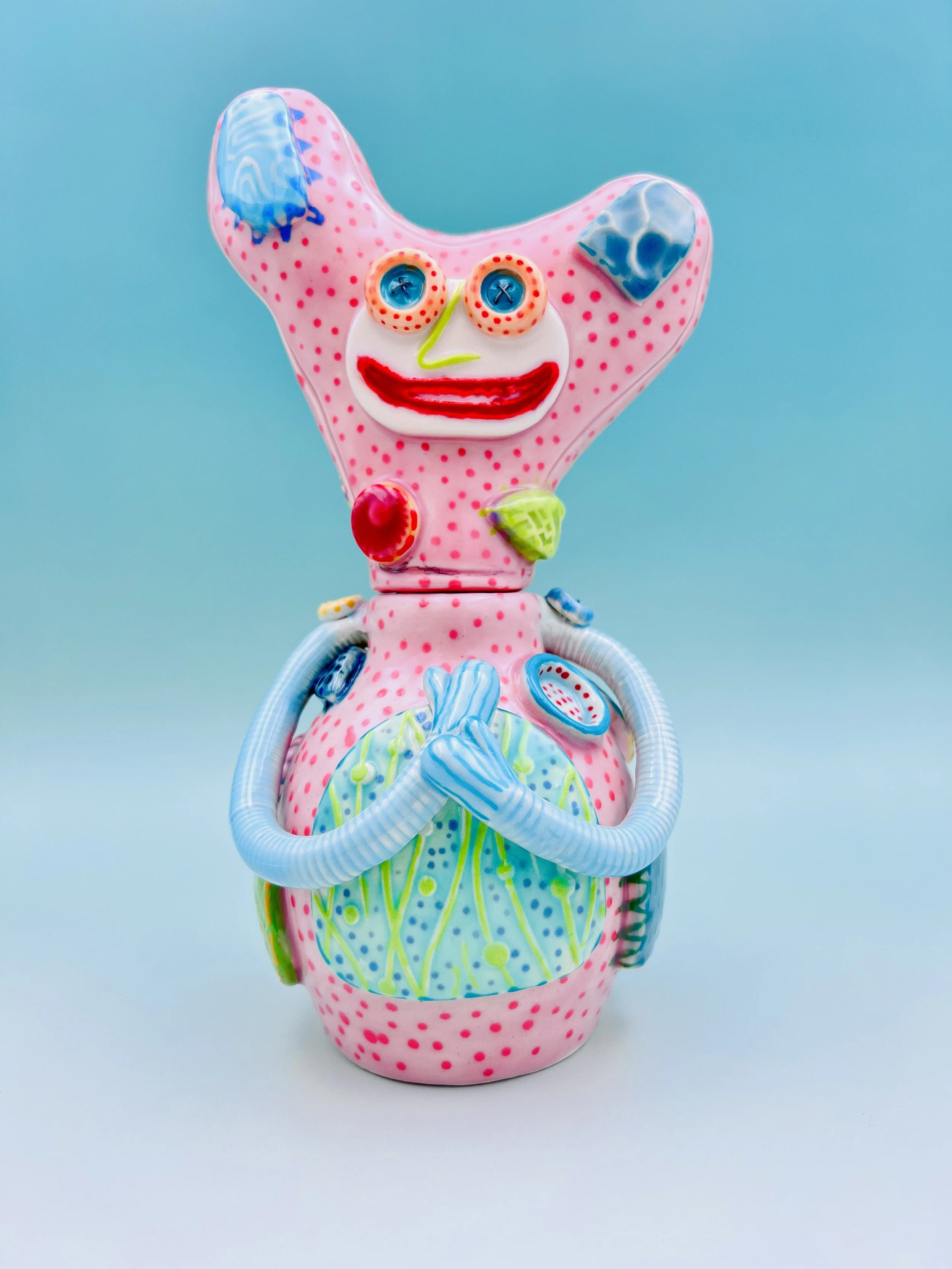 Colorful, whimsical ceramic figures called Gimmies with exaggerated facial features and various patterns, set against a gradient pastel background.