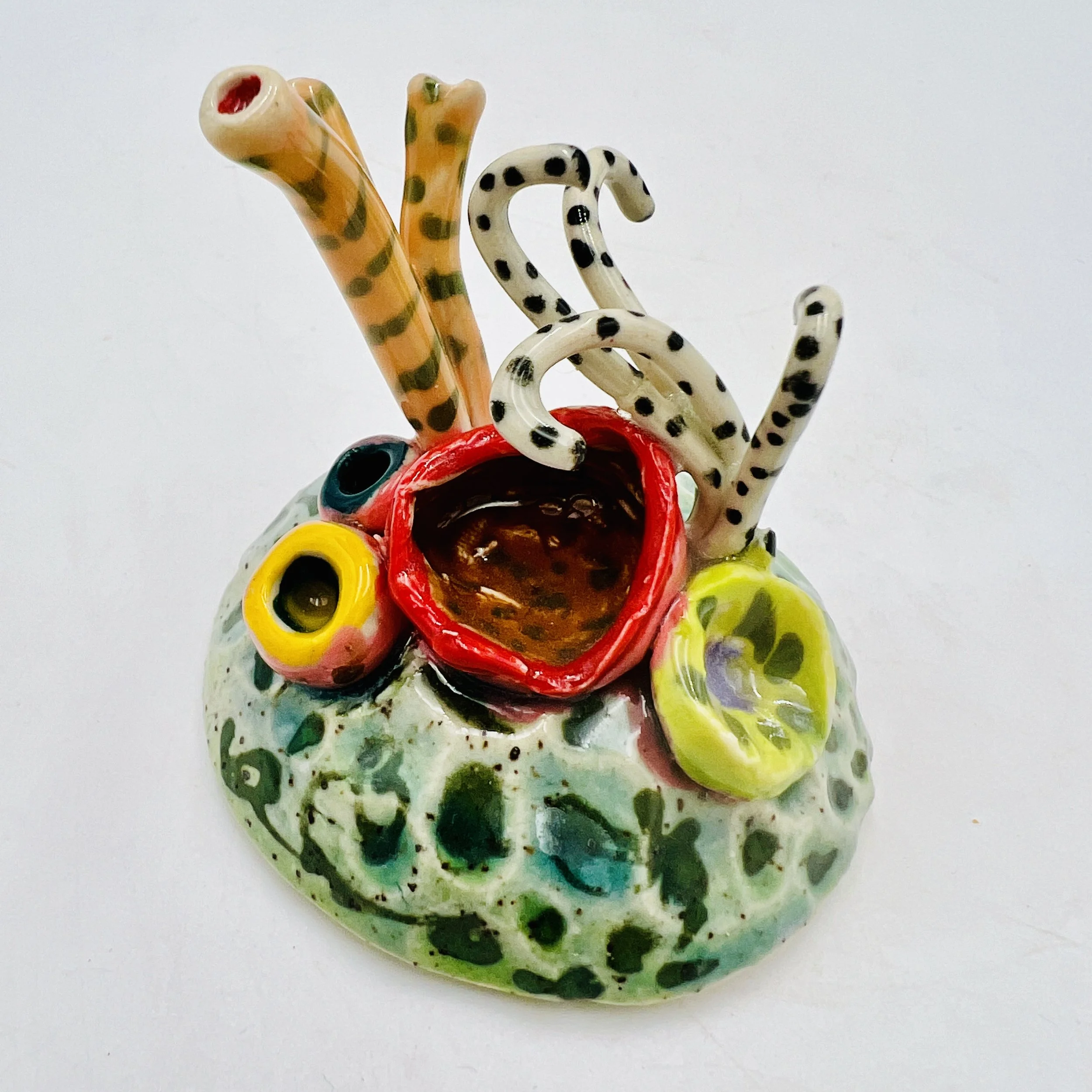 Colorful, textured clay sculptures resembling coral reefs arranged on a gradient background. Each piece has vibrant, intricate details, evoking a sense of ocean life.