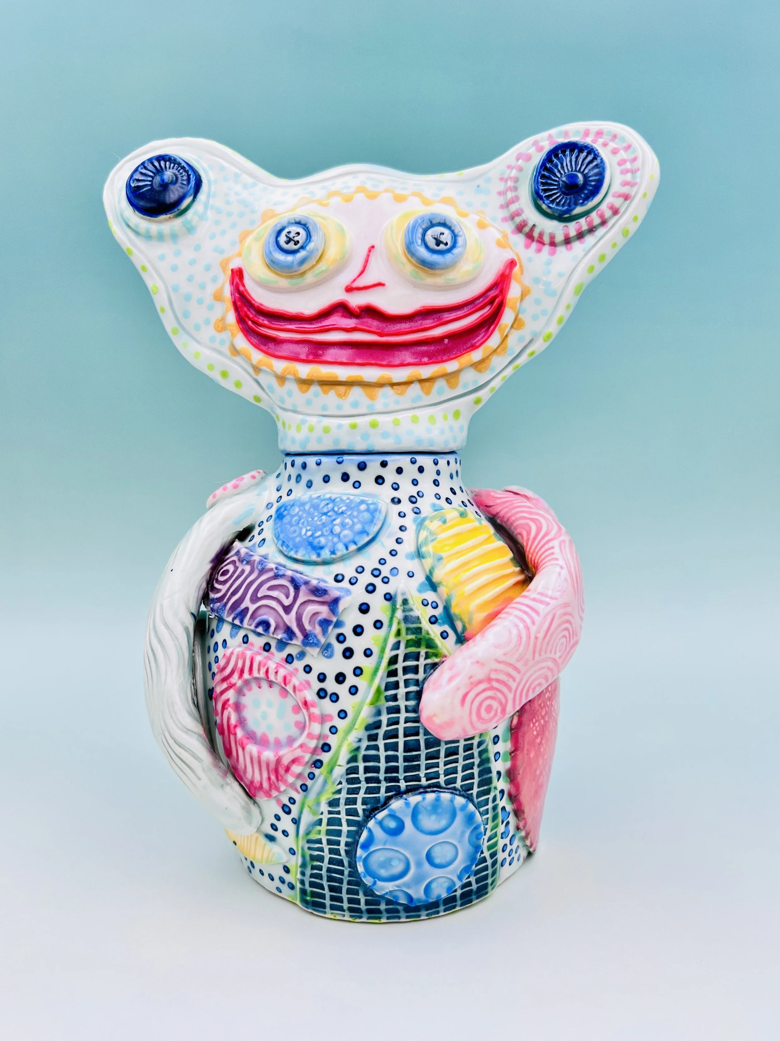 Colorful, whimsical ceramic figures called Gimmies with exaggerated facial features and various patterns, set against a gradient pastel background.