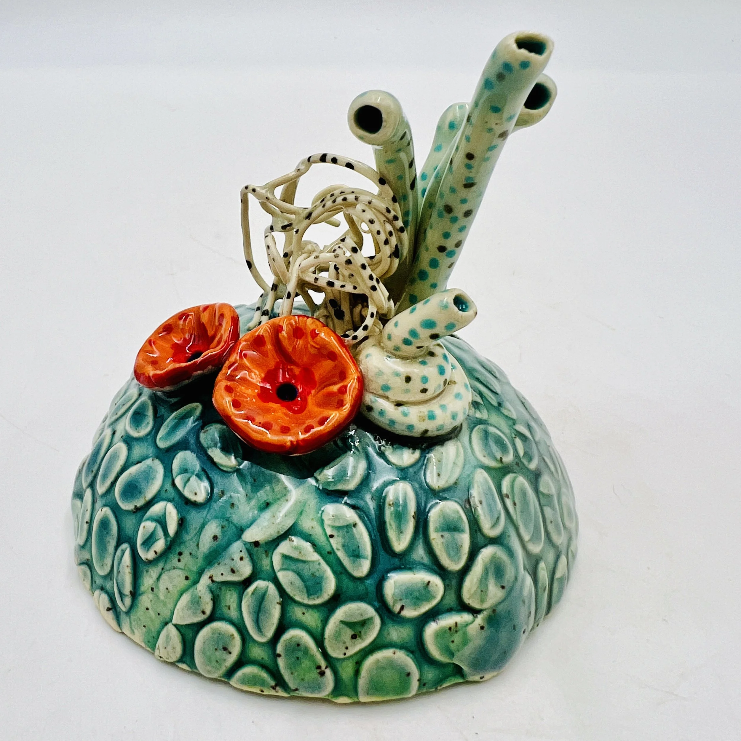 Colorful, textured clay sculptures resembling coral reefs arranged on a gradient background. Each piece has vibrant, intricate details, evoking a sense of ocean life.