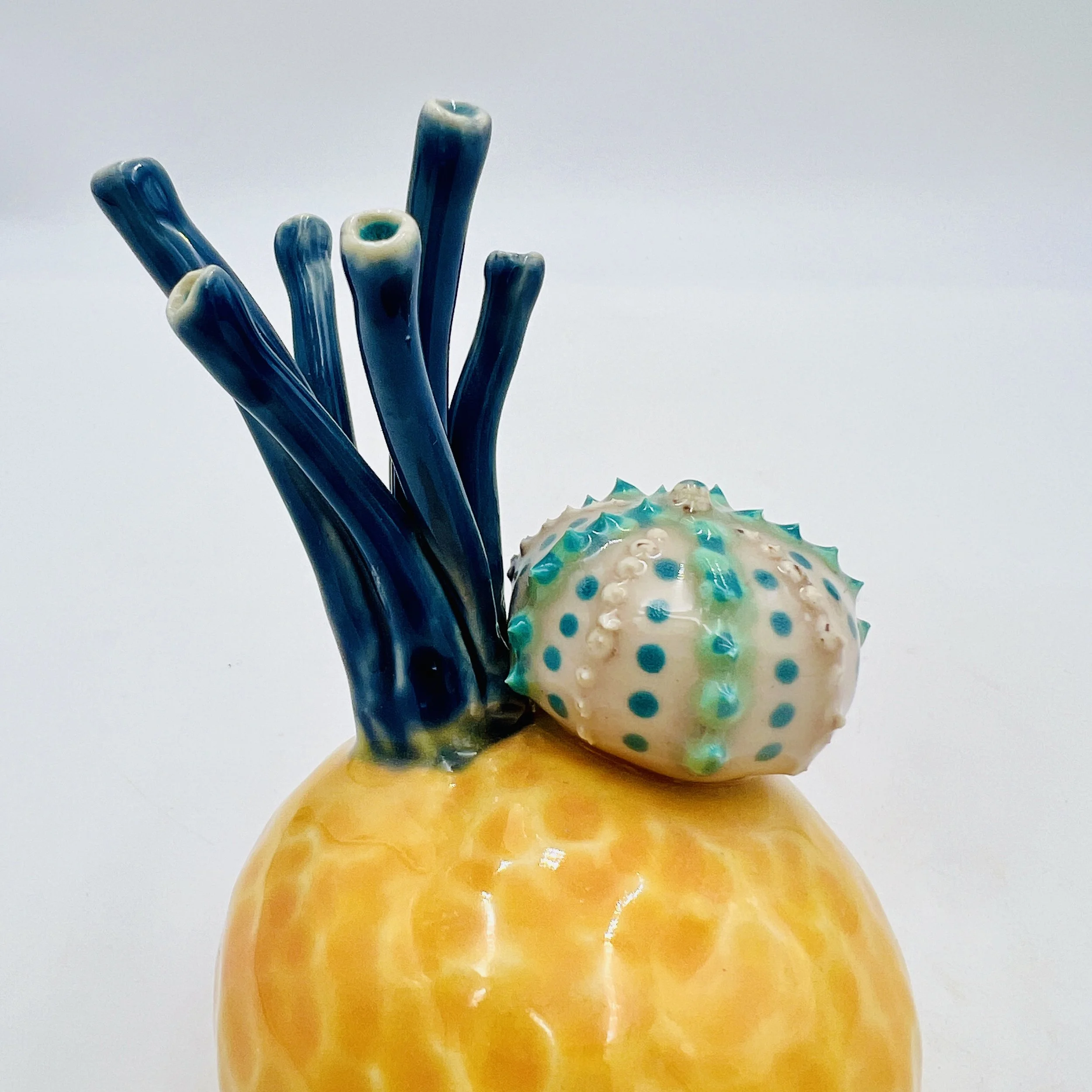 Colorful, textured clay sculptures resembling coral reefs arranged on a gradient background. Each piece has vibrant, intricate details, evoking a sense of ocean life.