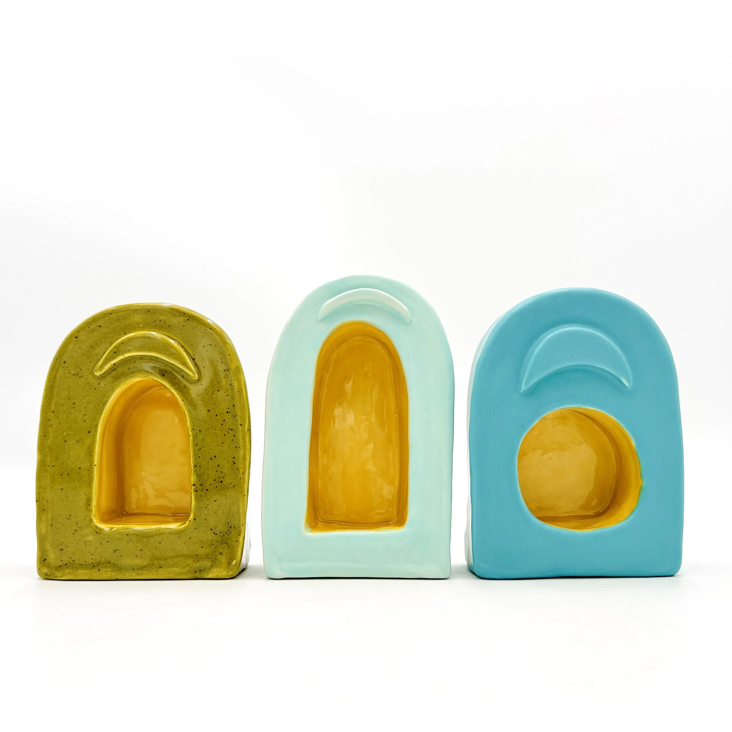 three small shrines, the left is green with a yellow inside, the middle is mint with a yellow inside and the right one is turquoise with yellow inside