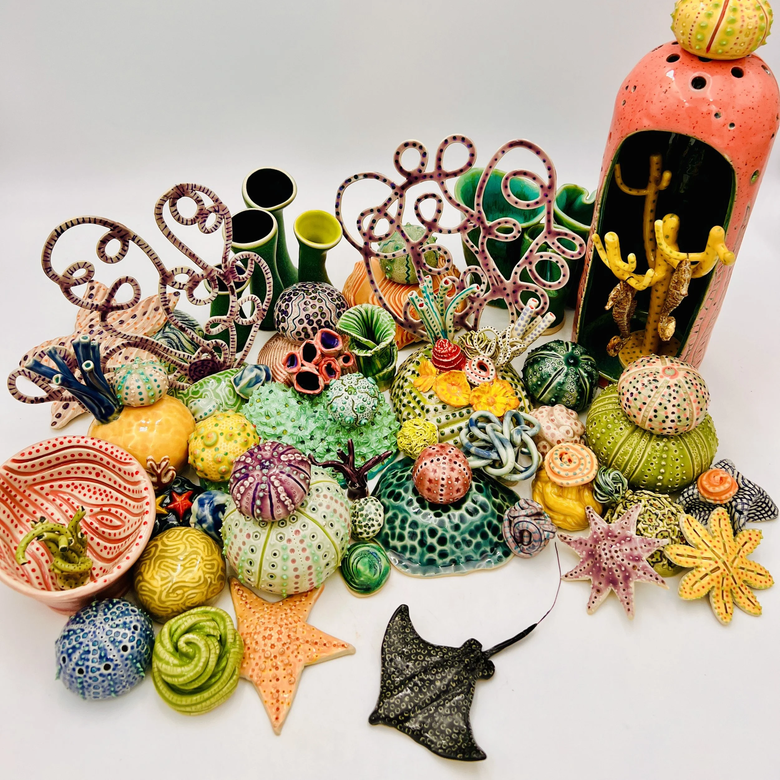 Colorful, textured clay sculptures resembling coral reefs arranged on a gradient background. Each piece has vibrant, intricate details, evoking a sense of ocean life.