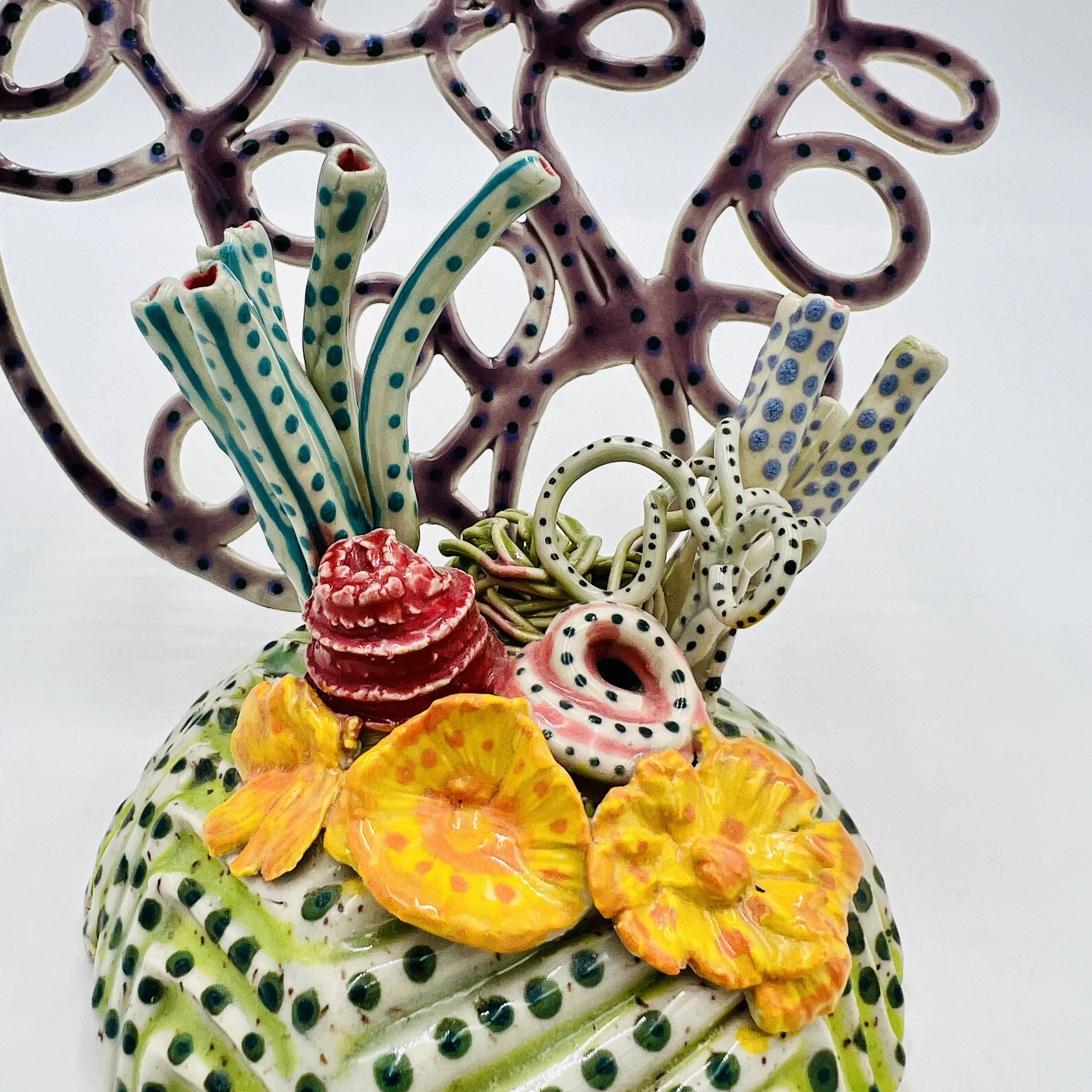 Colorful, textured clay sculptures resembling coral reefs arranged on a gradient background. Each piece has vibrant, intricate details, evoking a sense of ocean life.