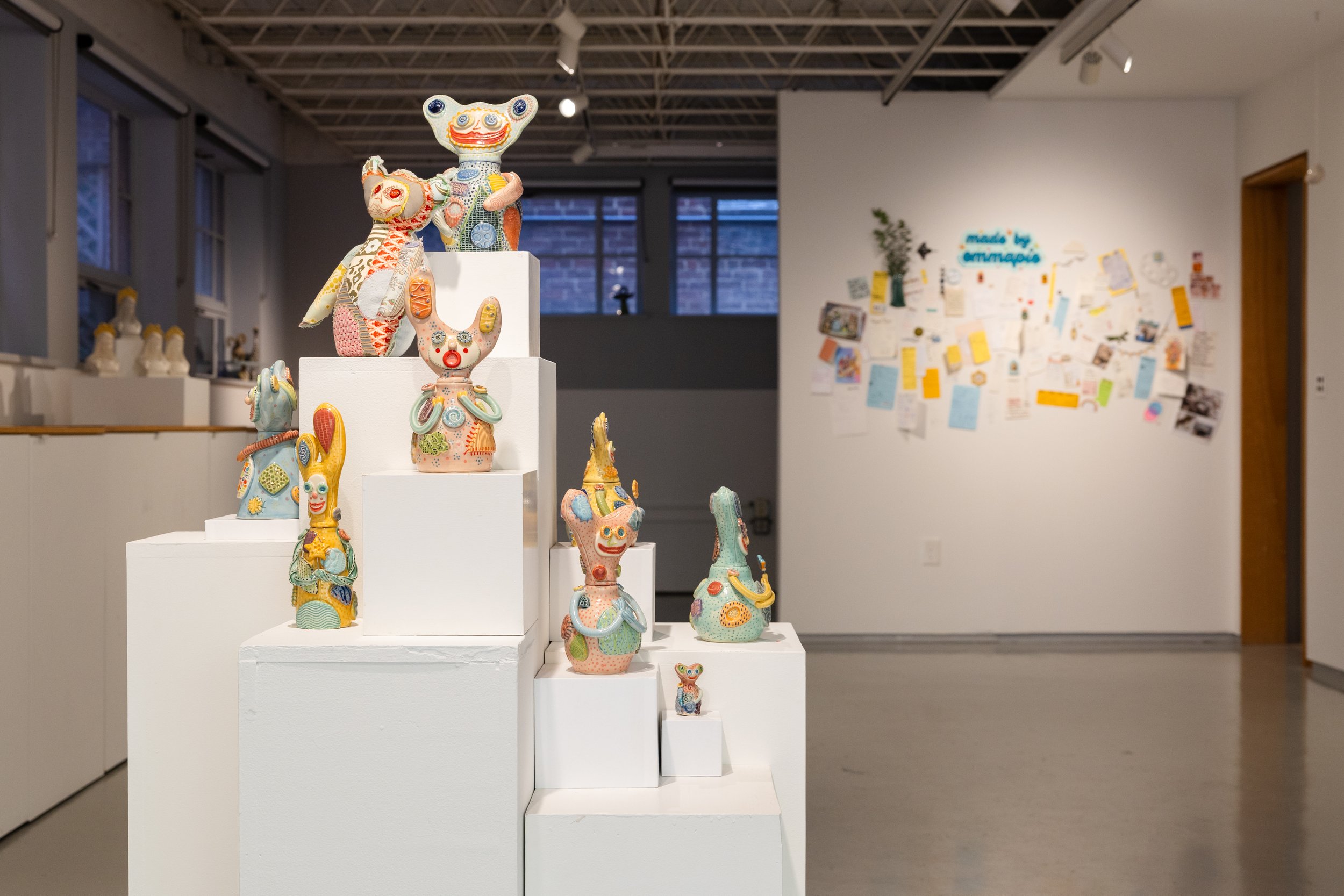 Colorful, hand-decorated animal sculptures stand on white pedestals in a modern gallery, creating a playful, whimsical exhibition against a gray wall.