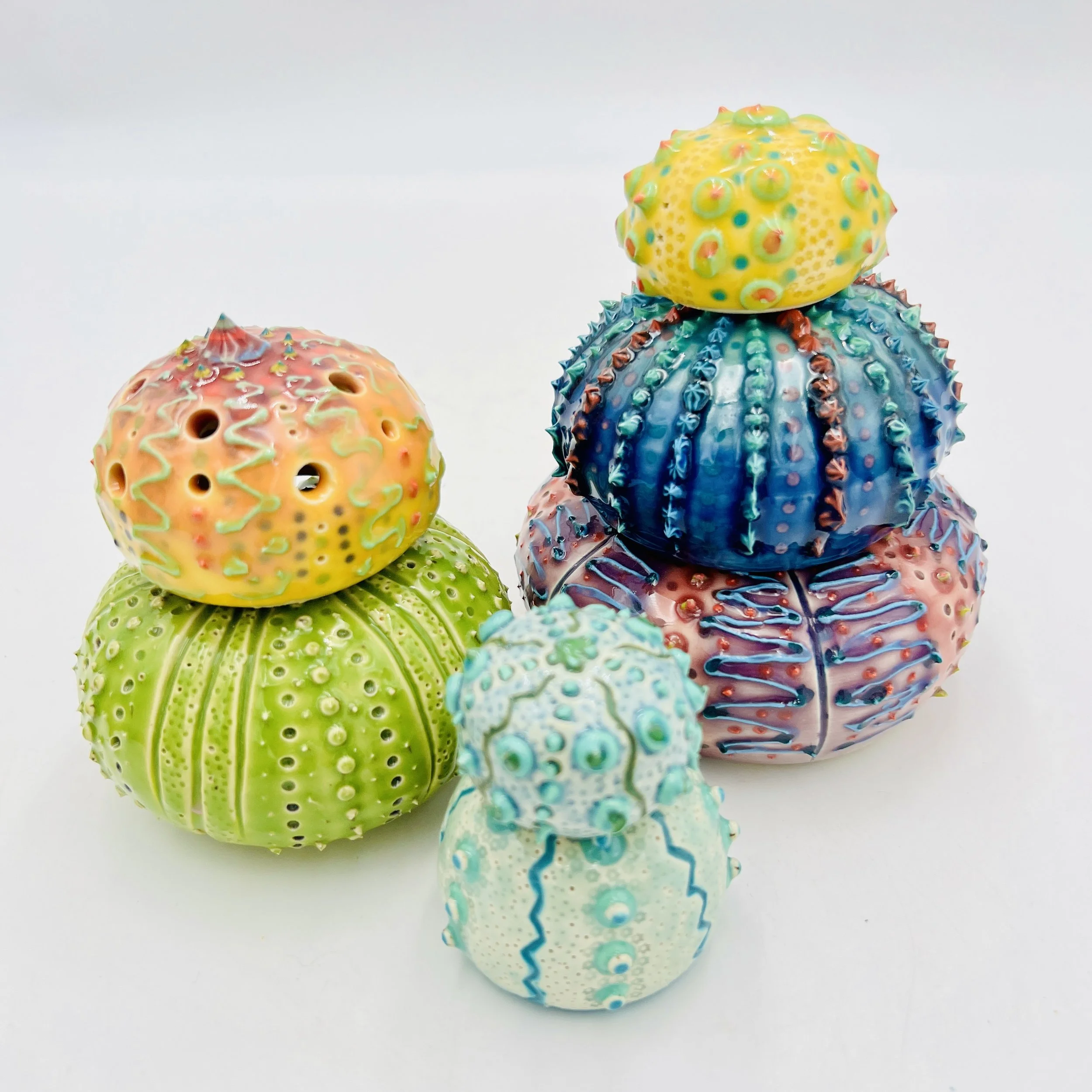 A group of colorful, intricately decorated sea urchin shells arranged on a white background.
