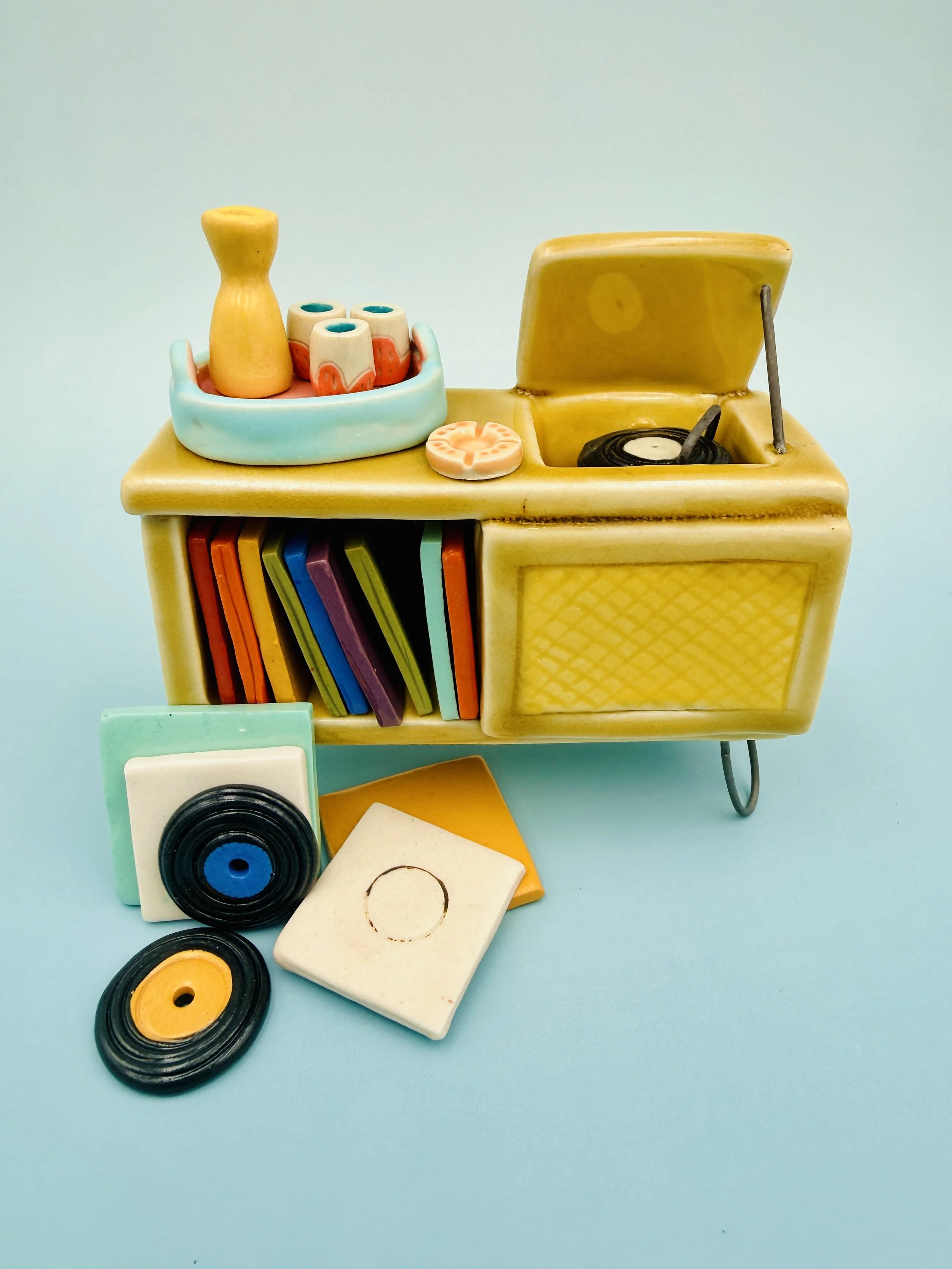 Ceramic figurine of a vintage record player with colorful record spines and a tray holding a yellow vase and decorative Malenka Made miniature pink tumblers.