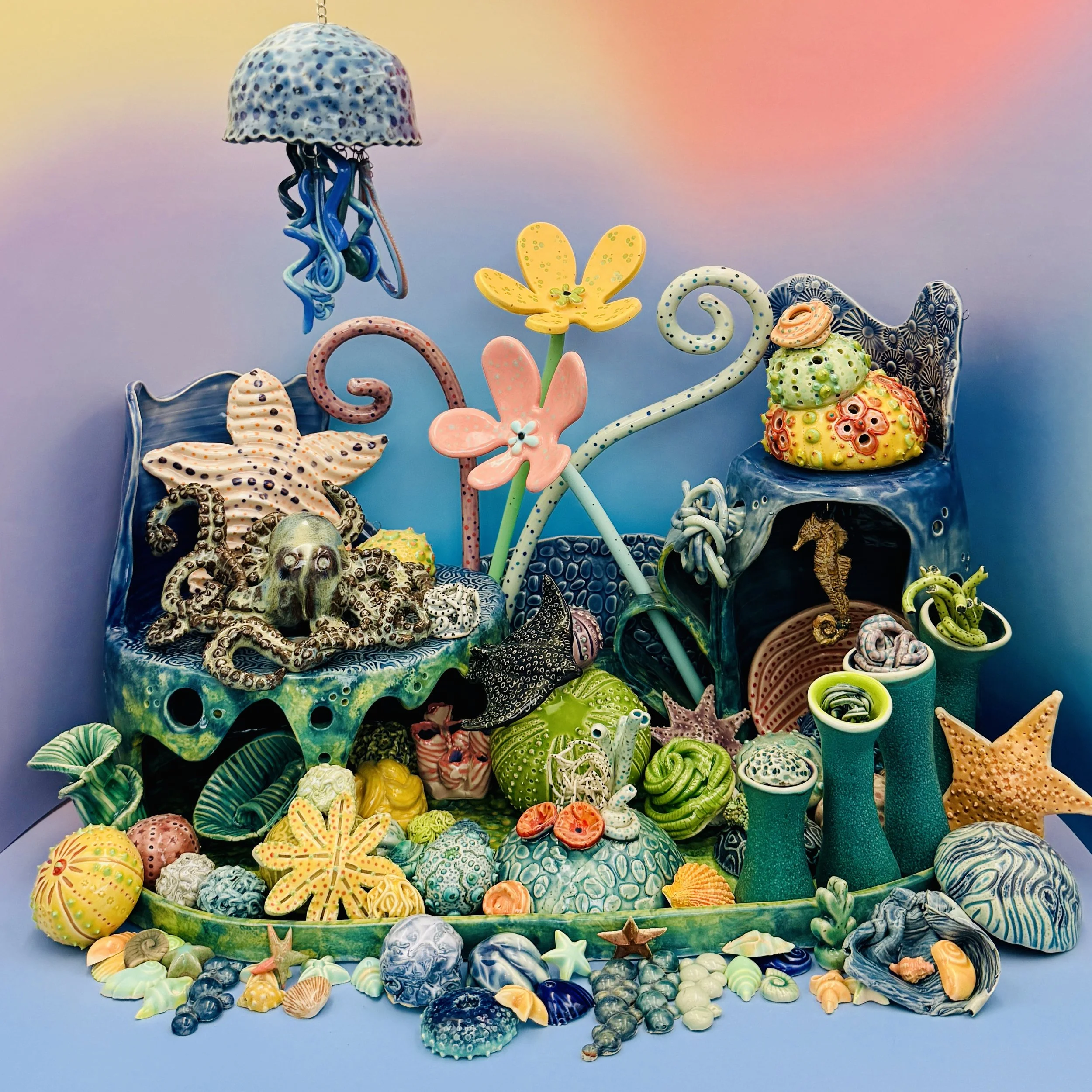 The image portrays an intricate underwater scene crafted from vibrant pottery, resembling a colorful coral reef. In the center, a detailed model of an octopus is nestled among green and blue corals, showcasing its textured body and large eyes. Surrou