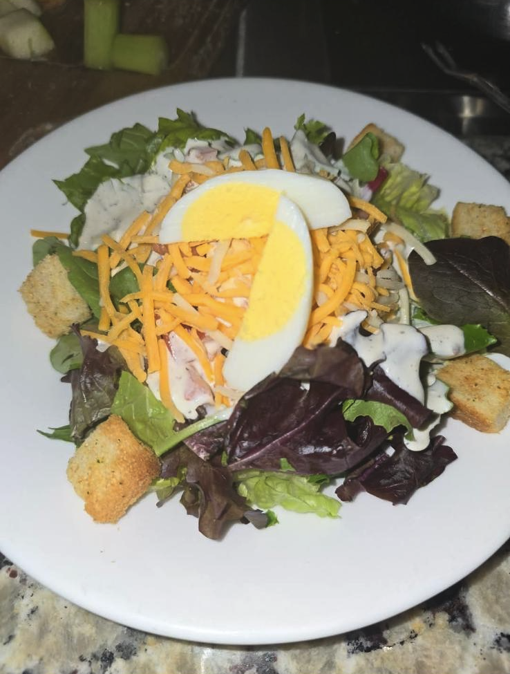 A plate of salad with mixed greens, shredded cheddar cheese, sliced hard-boiled egg, croutons, and creamy dressing.