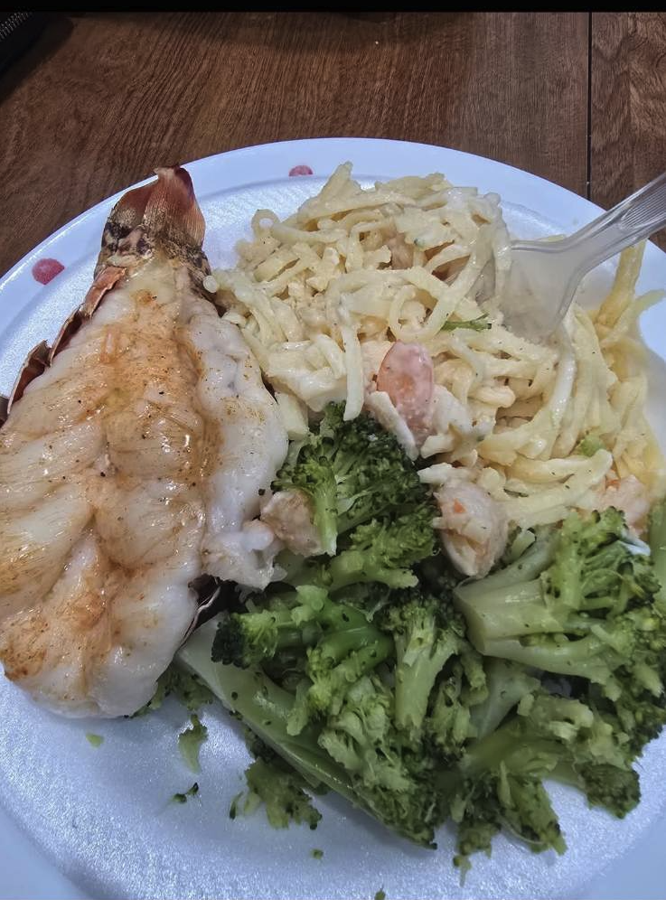 Plate with cooked shrimp, macaroni salad, and steamed broccoli on a wooden table