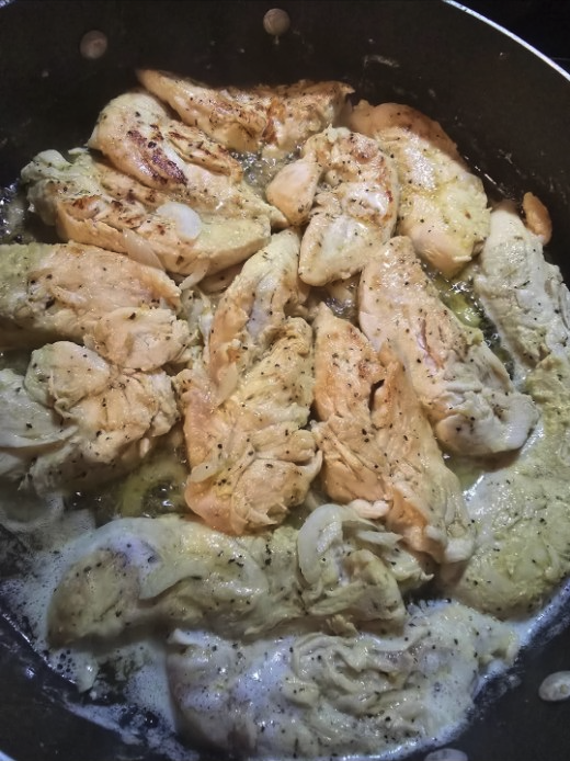 Cooking chicken in a skillet, with pieces of chicken browning and frying in melted butter or oil.