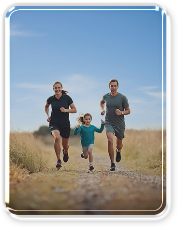 Family running together on a dirt path in an open field under a blue sky.