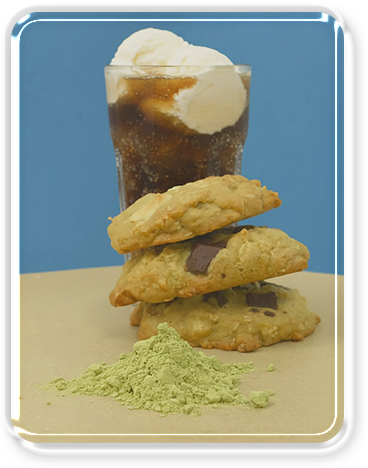 A glass of cola with ice cream on top, three chocolate chip cookies stacked, green powdered matcha, and a blue background.