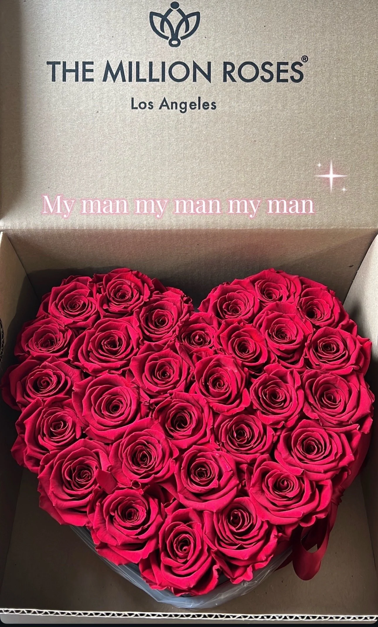 A heart-shaped box filled with red roses. The box is inside a larger box with the label 'The Million Roses Los Angeles' on the lid, and a slogan 'My man my man my man' written in pink.