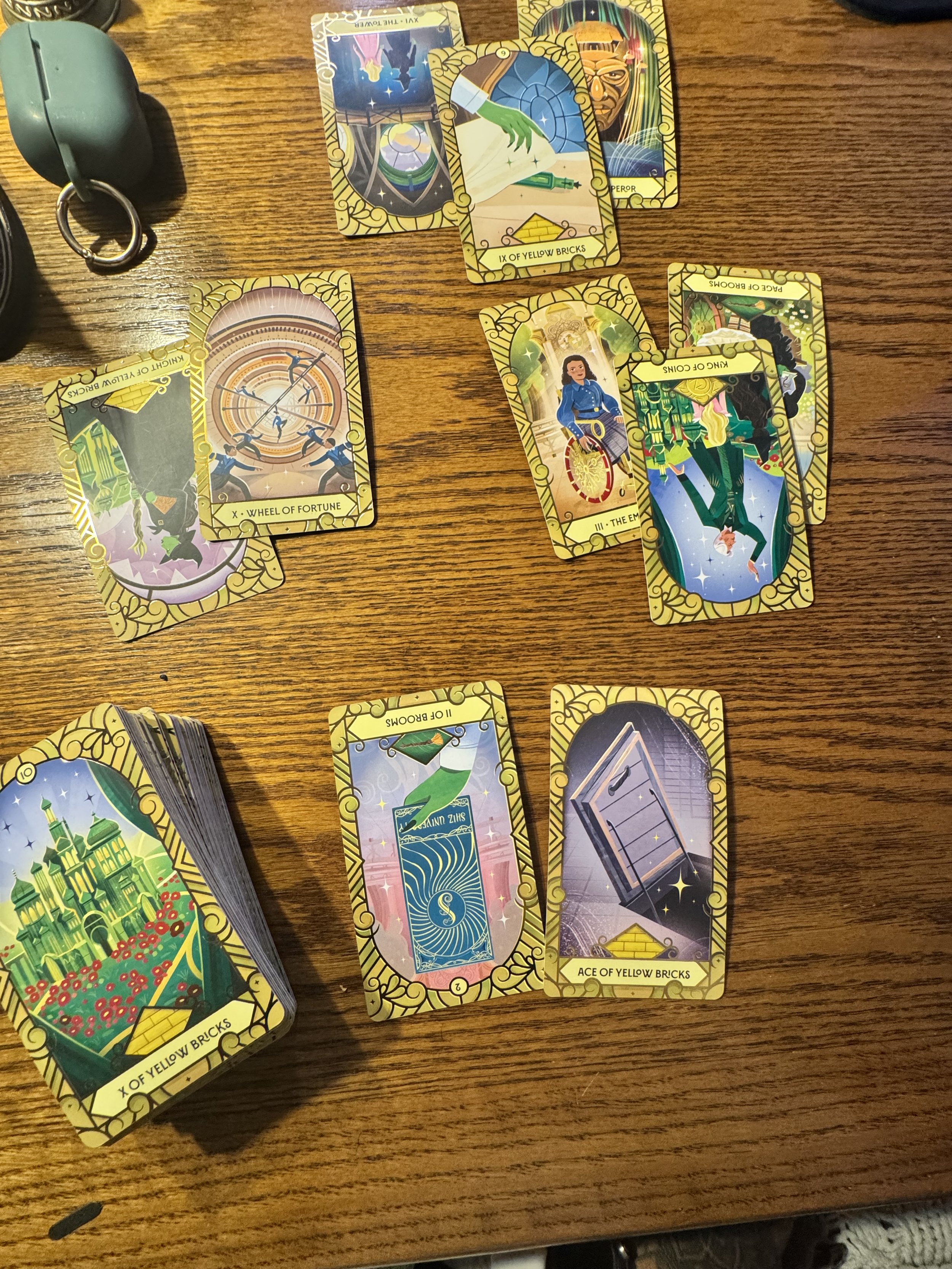 Various colorful tarot cards laid out on a wooden table, including cards titled 'Wheel of Fortune,' 'X of Yellow Bricks,' 'Ace of Yellow Bricks,' 'King of Cups,' 'Peril,' and 'The Empress.'