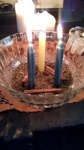 A cake with lit birthday candles, some candles are blue and others are yellow, surrounded by a glass bowl with decorative stones.