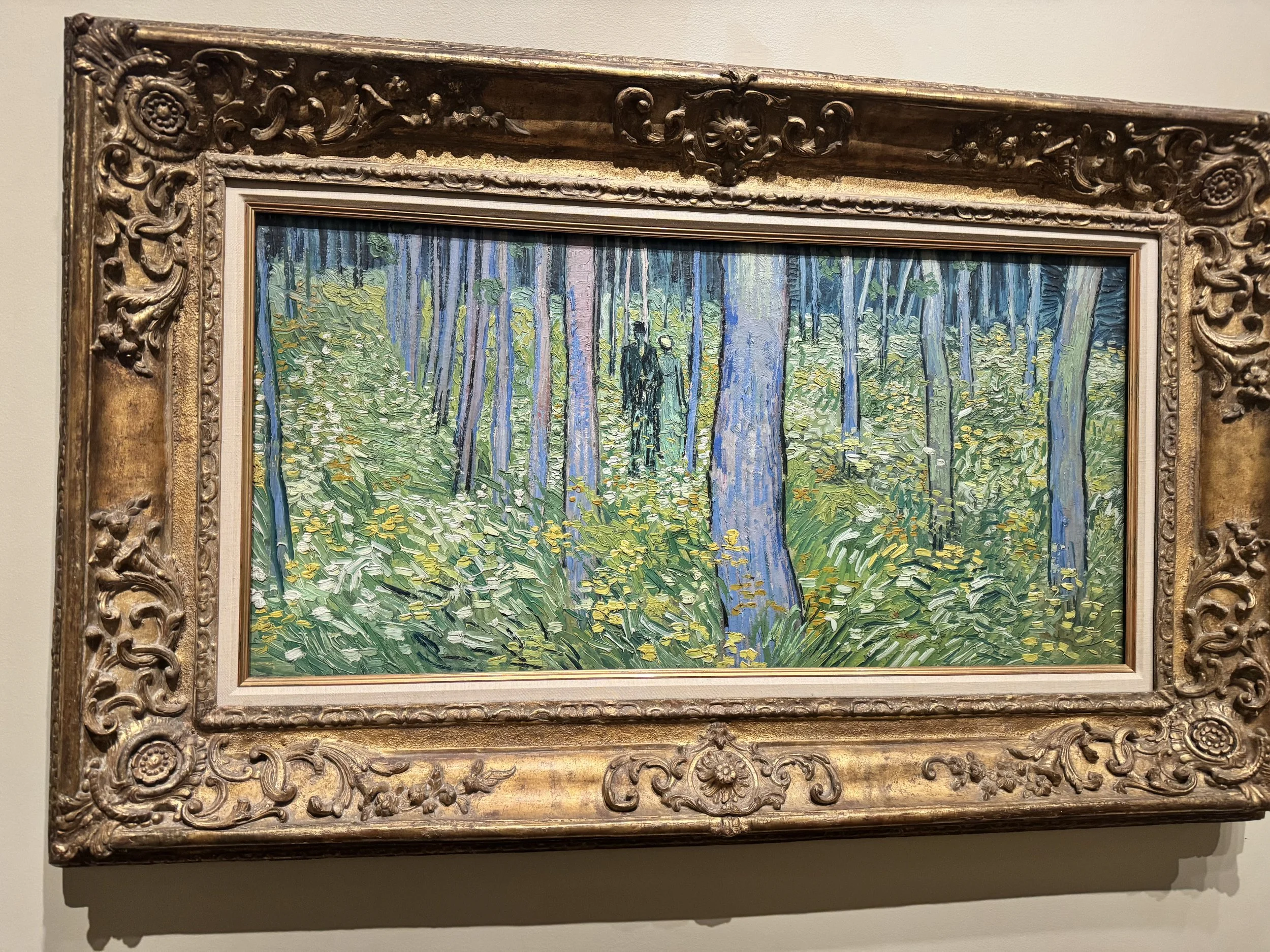 A framed painting of a forest scene with trees and foliage, featuring impressionist brushstrokes and vivid colors, encased in an ornate, gilded frame.