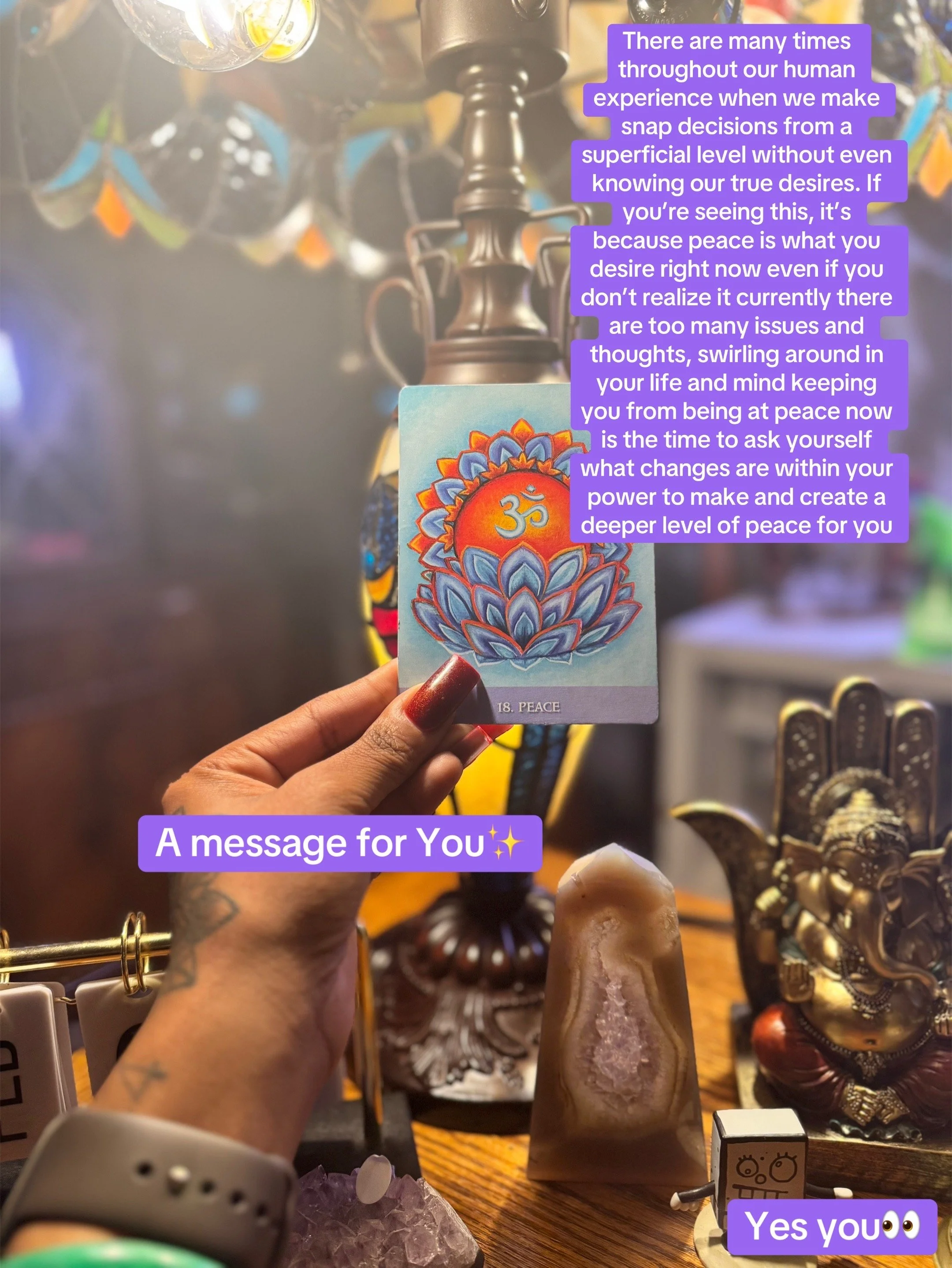 A person holds a card labeled 'Peace' with a colorful floral design and the 'Om' symbol. The background features spiritual and decorative items, including Buddha statues, figurines, and jewelry, on a wooden surface. Purple text overlays the image, al