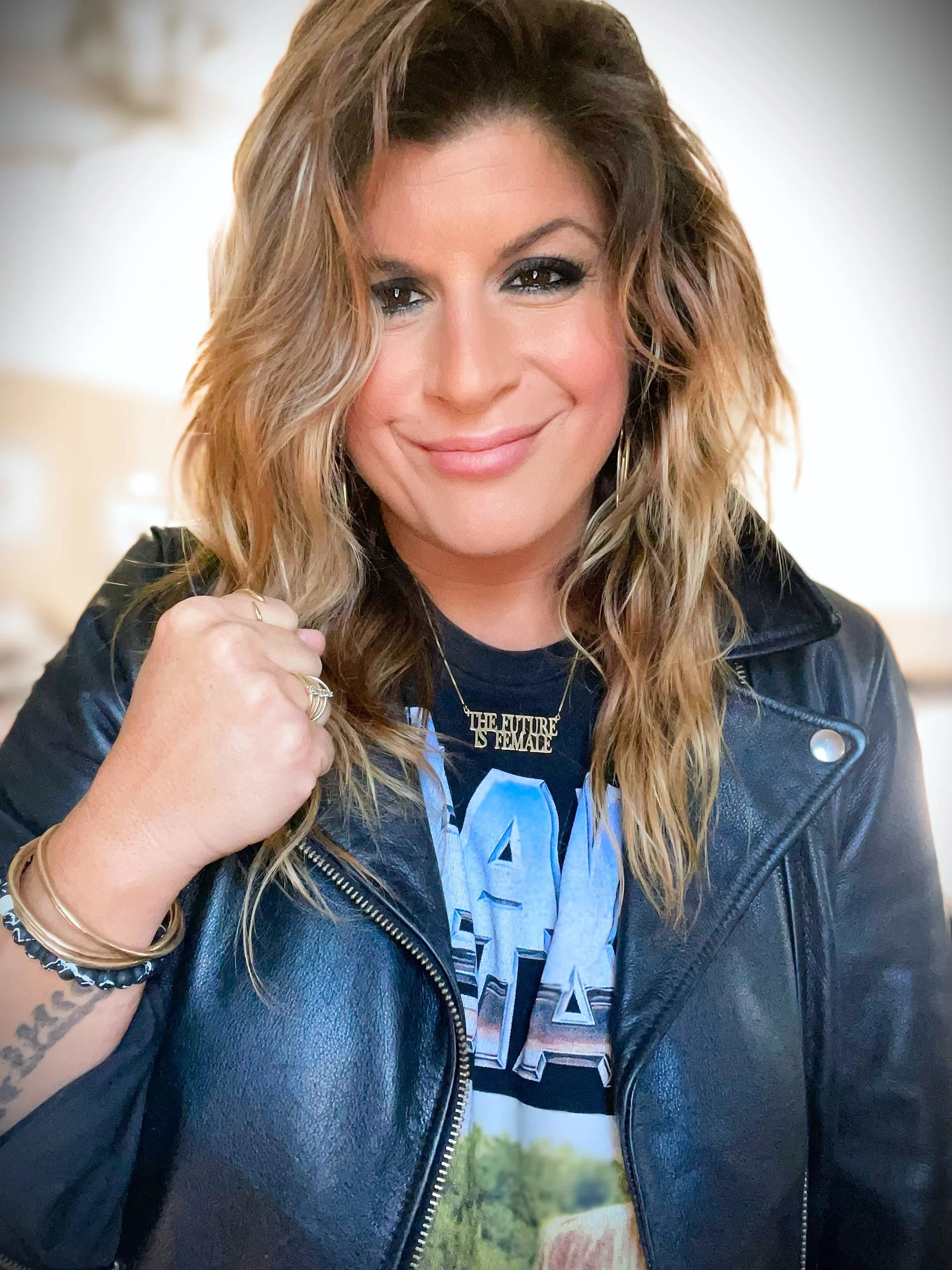 Women's empowerment expert Dr. Alice Atalanta feeling empowered and strong with long hair wearing a leather jacket and graphic t-shirt, smiling.