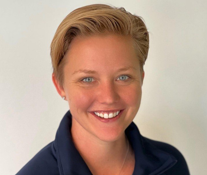 Portrait of Stef Fee, USA Field Hockey Olympian and Duke University Athlete and coach of Powerhouse Field Hockey, with short hair wearing a dark collared shirt against a neutral background.