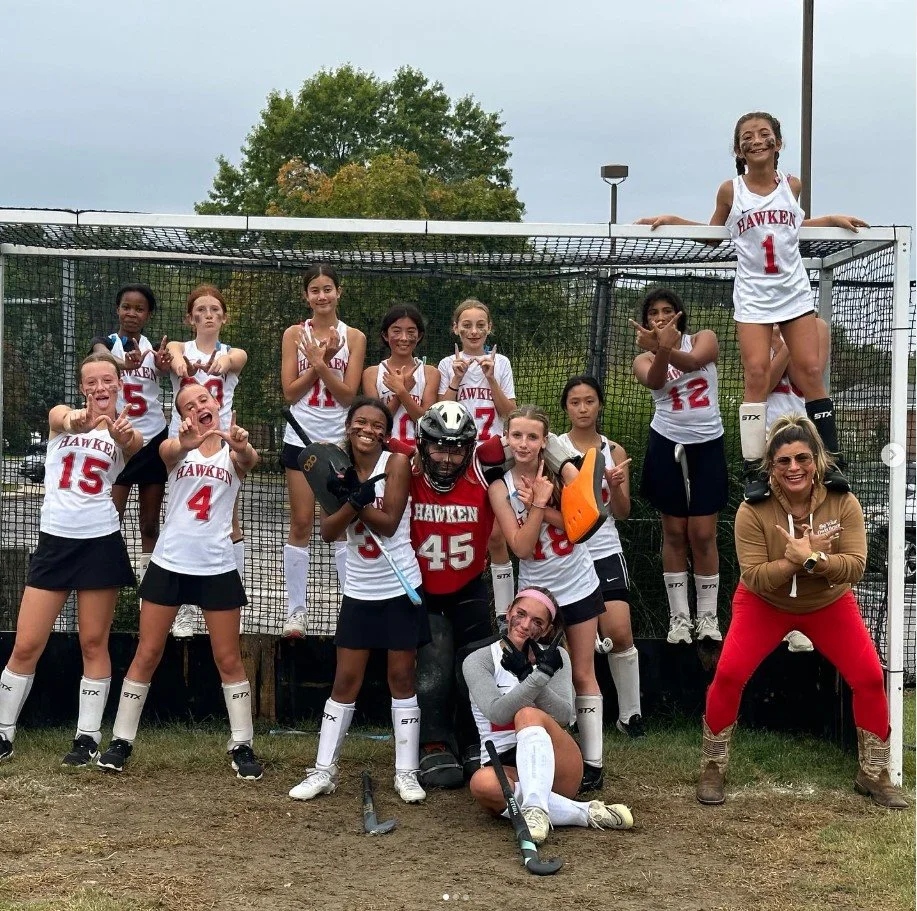 Women's empowerment expert Dr. Alice Atlanta pictured with the field hockey team she coaches inside a goal as the girls feel stronng, empowered, and  joyful celebrating a win and an undefeated season.